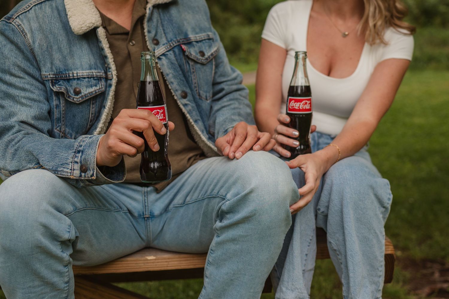 Two people in jeans sitting outdoors with Coca-Cola bottles on a warm summer afternoon.