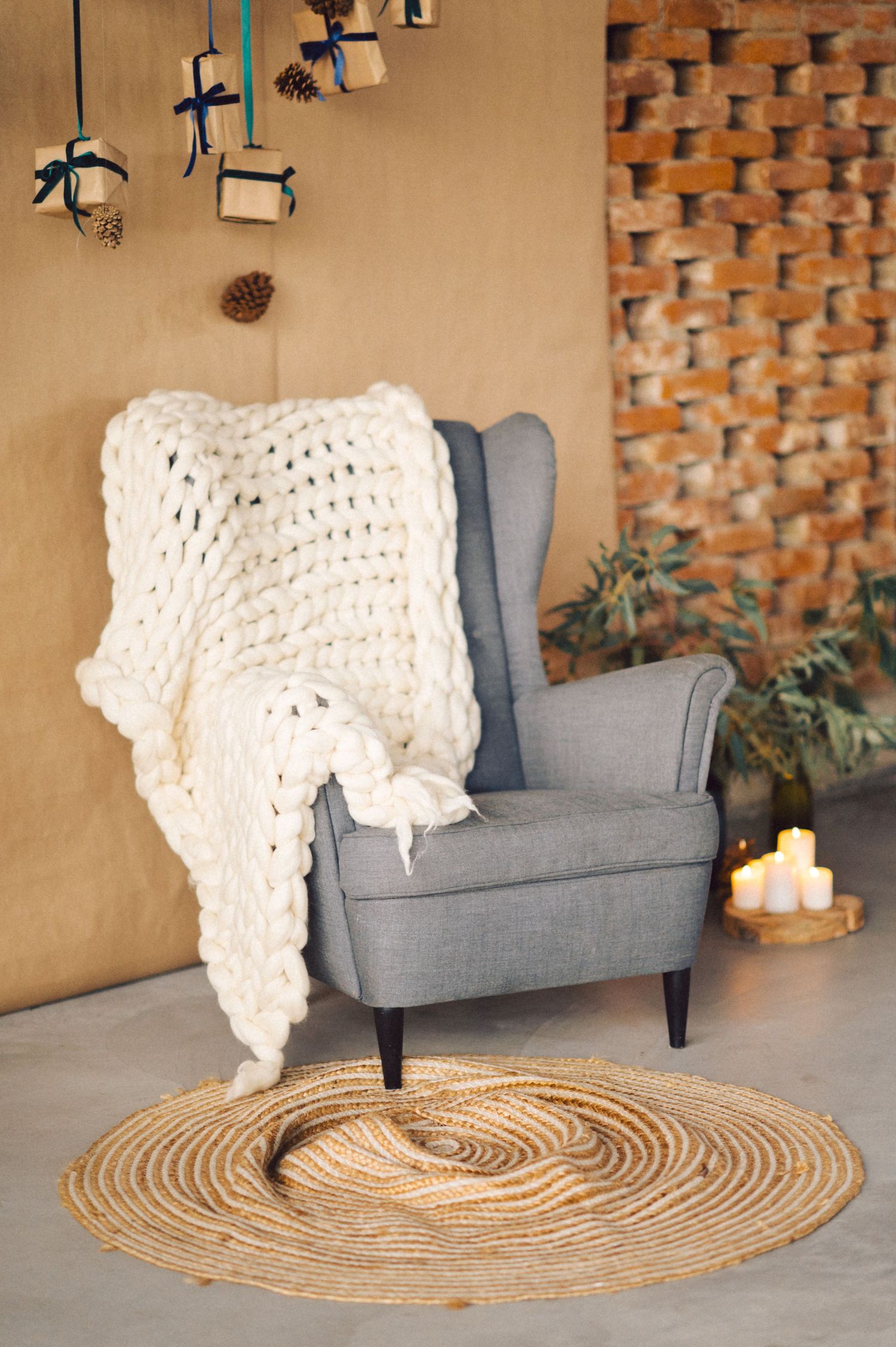 A chunky cream knit throw blanket drapes over a modern gray wingback chair with a round jute rug beneath.