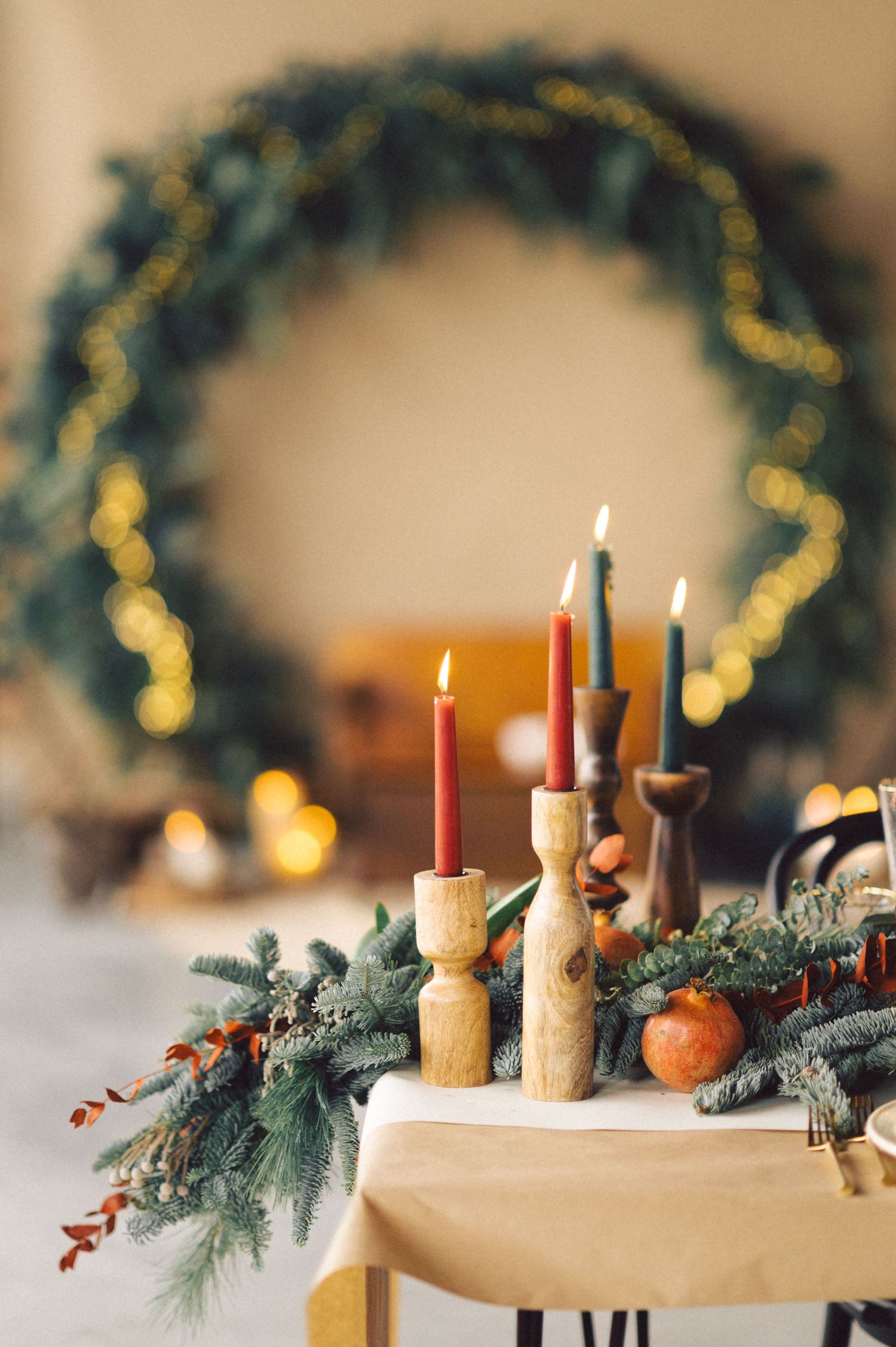 Lit candles in wooden holders with evergreen branches and holiday wreath decoration create a cozy Christmas atmosphere.