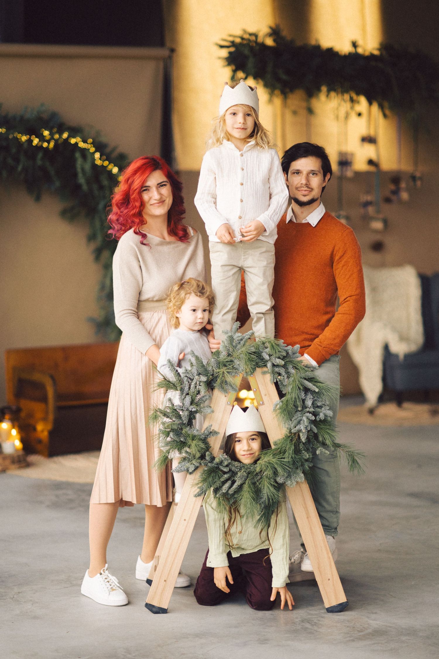 Family poses together with Christmas wreath and holiday decorations in a cozy indoor setting.