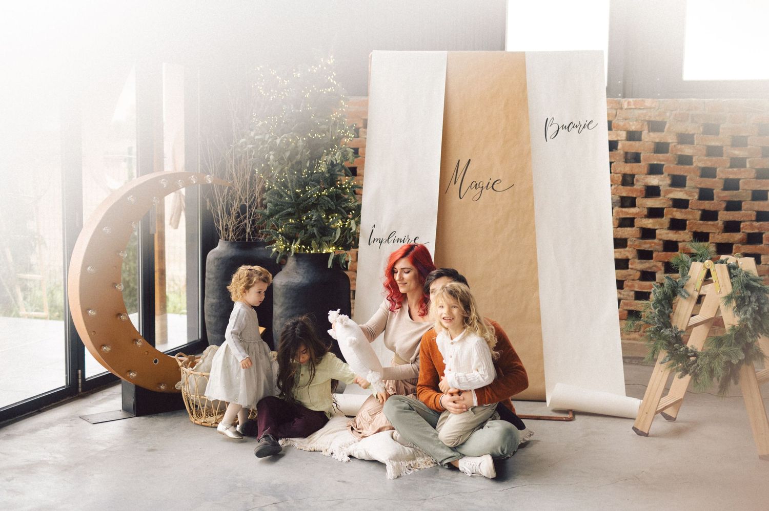 Family sits together in a whimsical nursery setup with decorative moon crescent and paper backdrop in natural lighting.