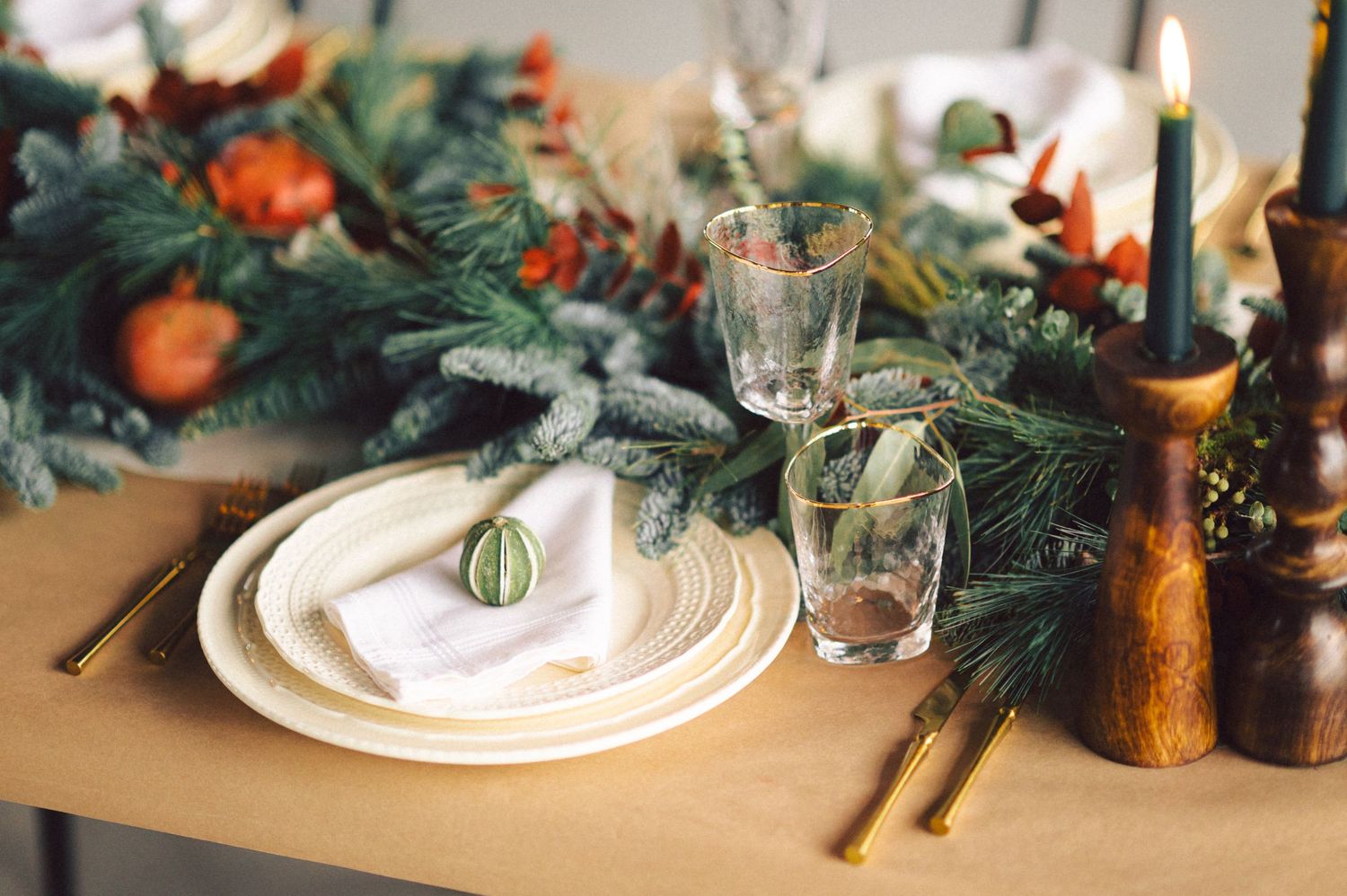 A festive table setting with evergreen garlands, white plates, antique candlesticks and clementines for holiday decor.