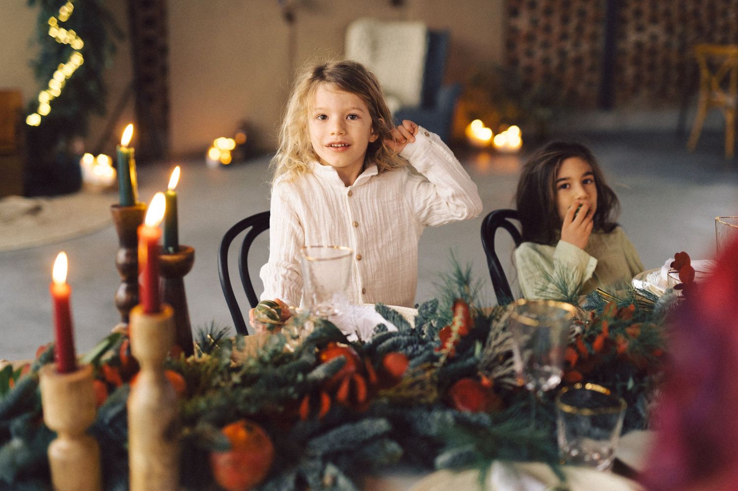 A festive holiday table setting with candles, greenery, and people gathered for a Christmas celebration.
