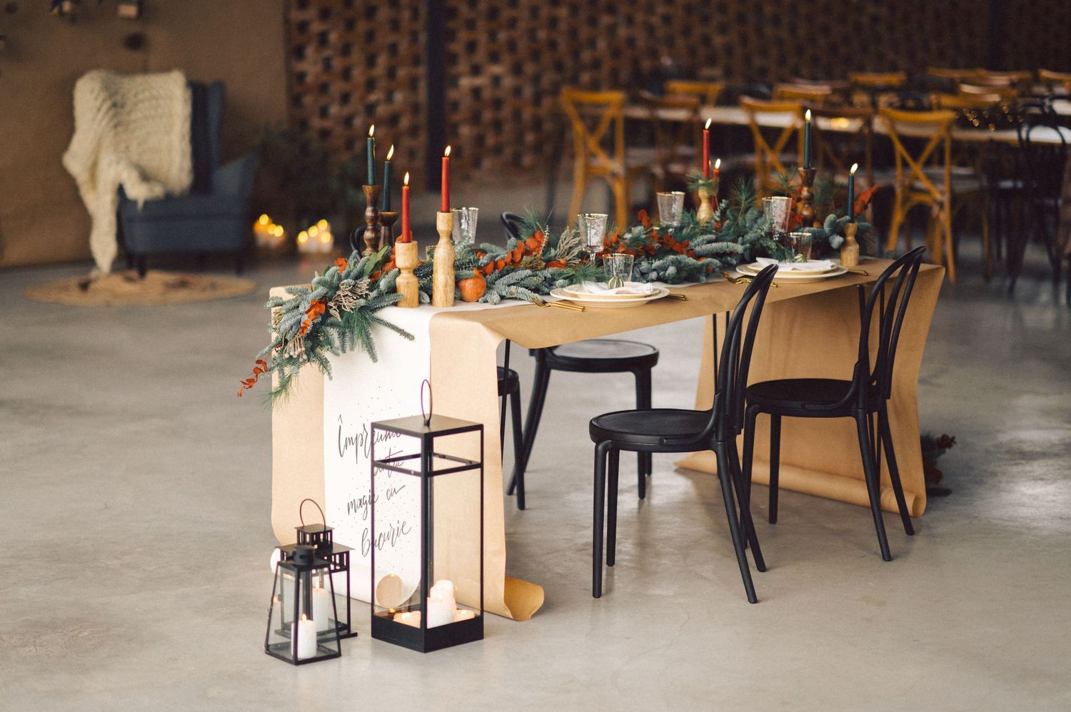 Modern industrial wedding reception table setup with greenery garland, lanterns and mixed black and gold chairs.
