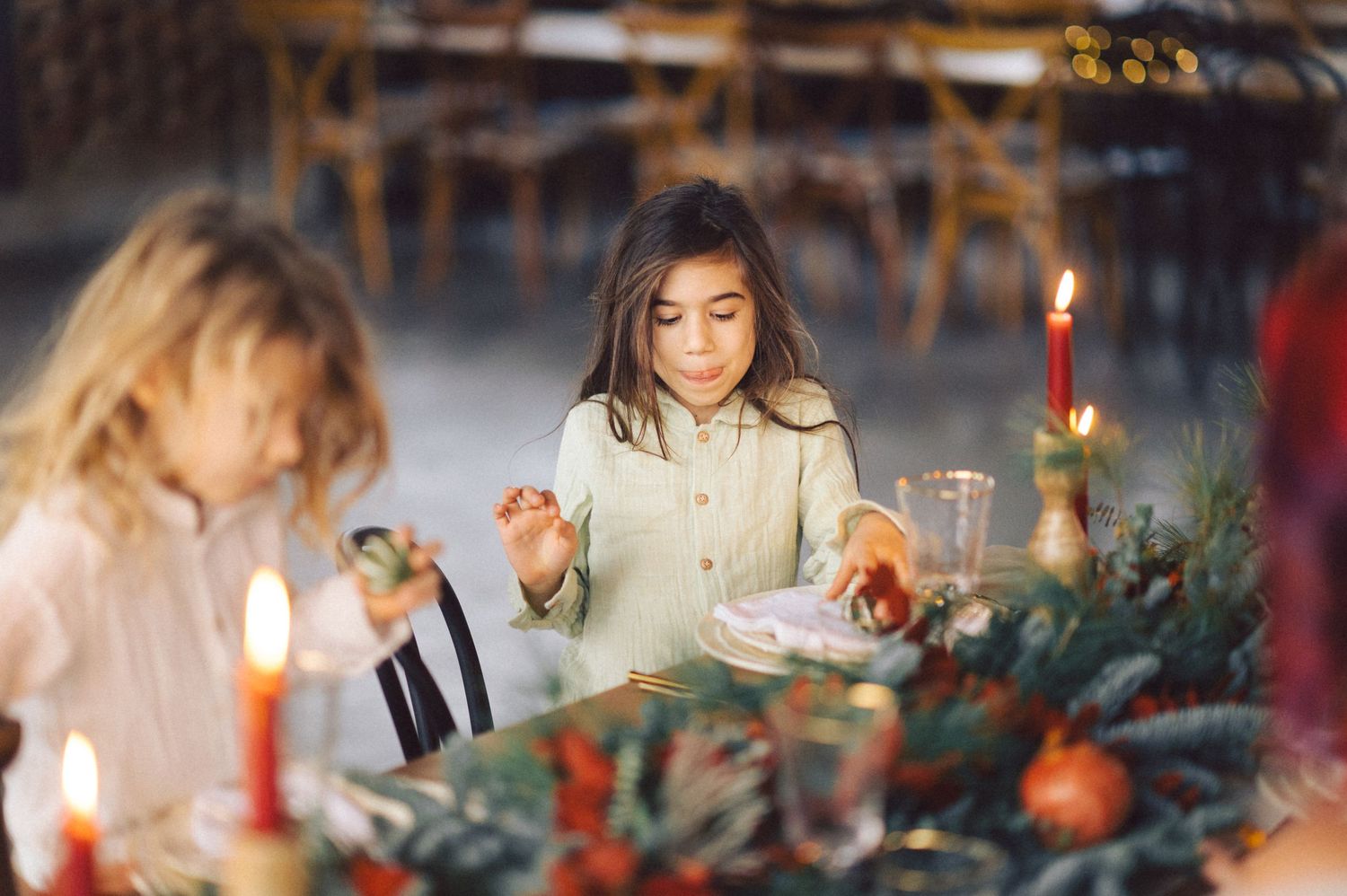 People enjoy a festive holiday dinner at a table decorated with red candles and evergreen branches.