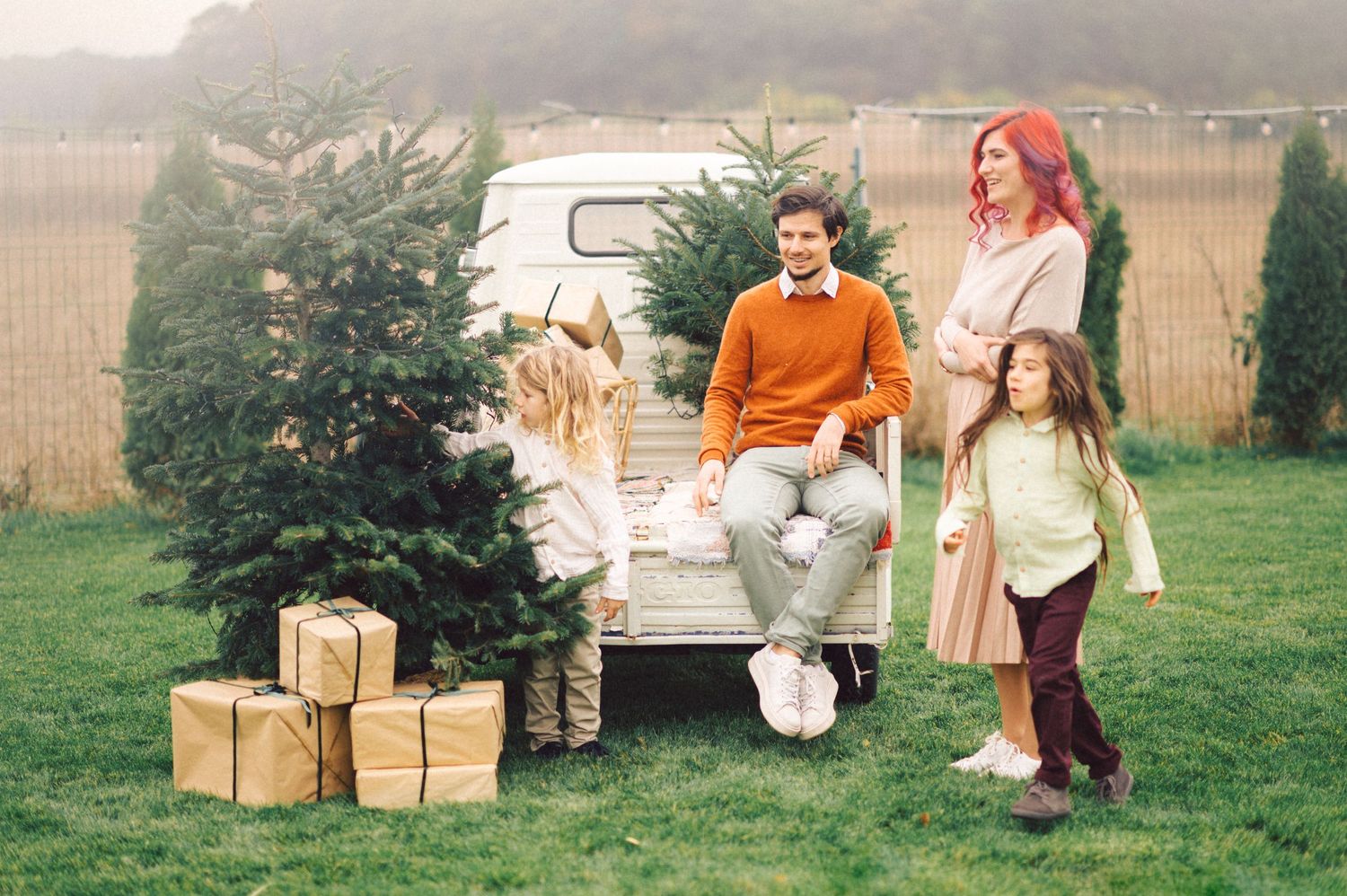 A group stands by a vintage white van with holiday packages and a small evergreen tree on a foggy day.