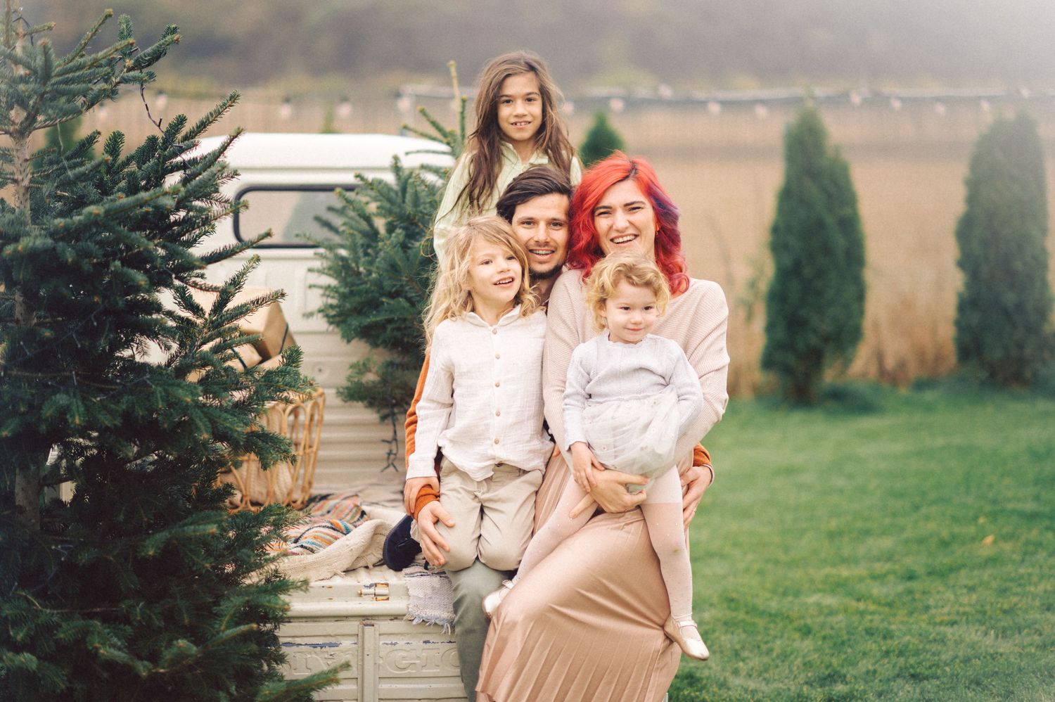 Family poses together for a portrait outdoors near evergreen trees in a rustic countryside setting.