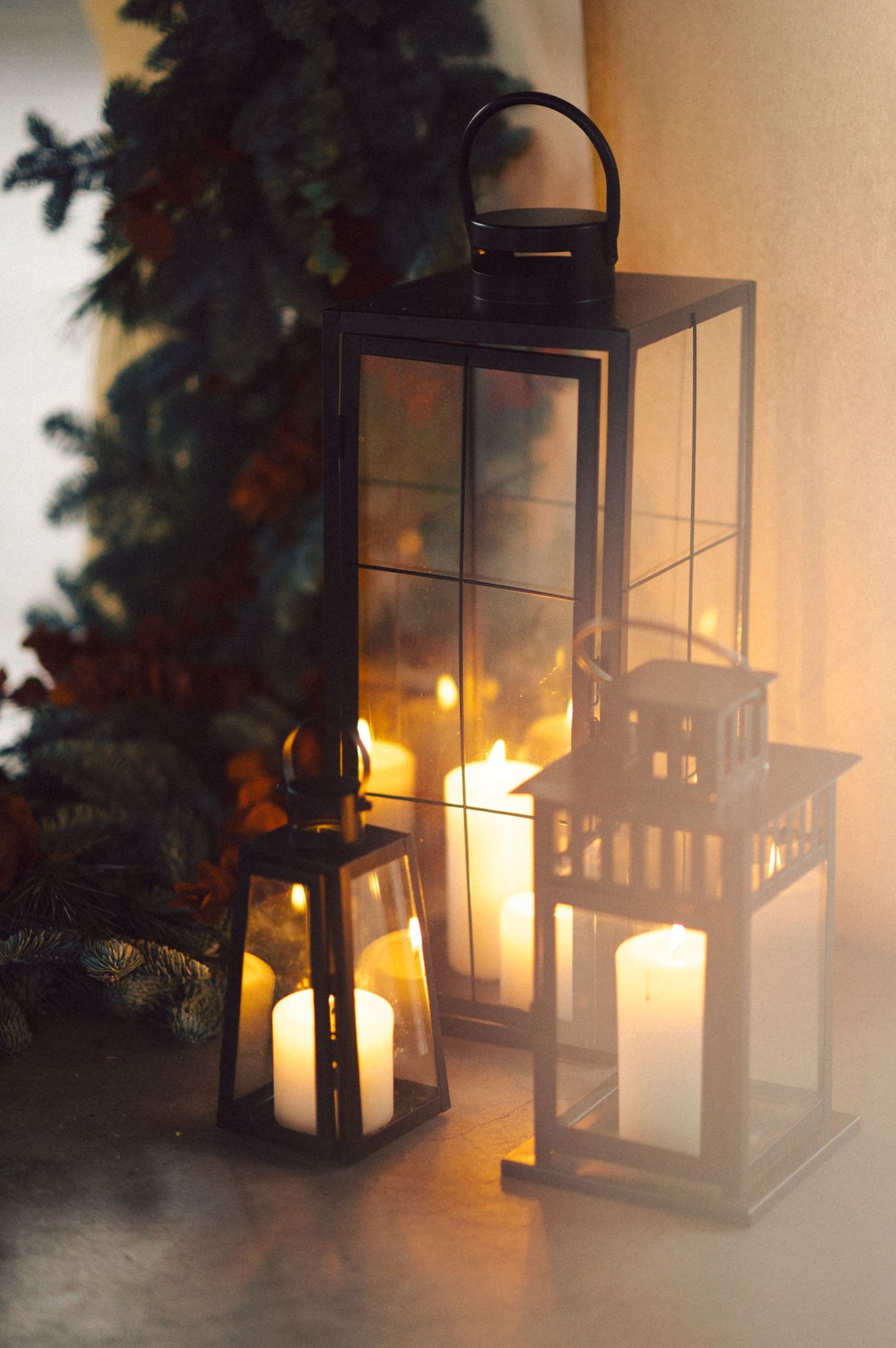 Glowing lanterns with candles create a cozy holiday atmosphere near evergreen Christmas decorations.