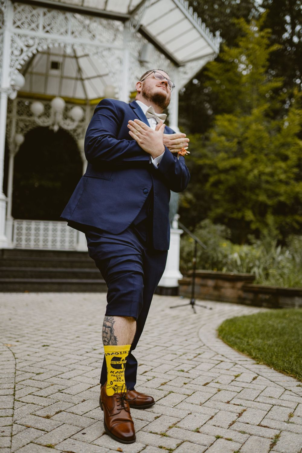 Person in navy suit shows emotion with hand on chest, wearing yellow socks at outdoor venue.