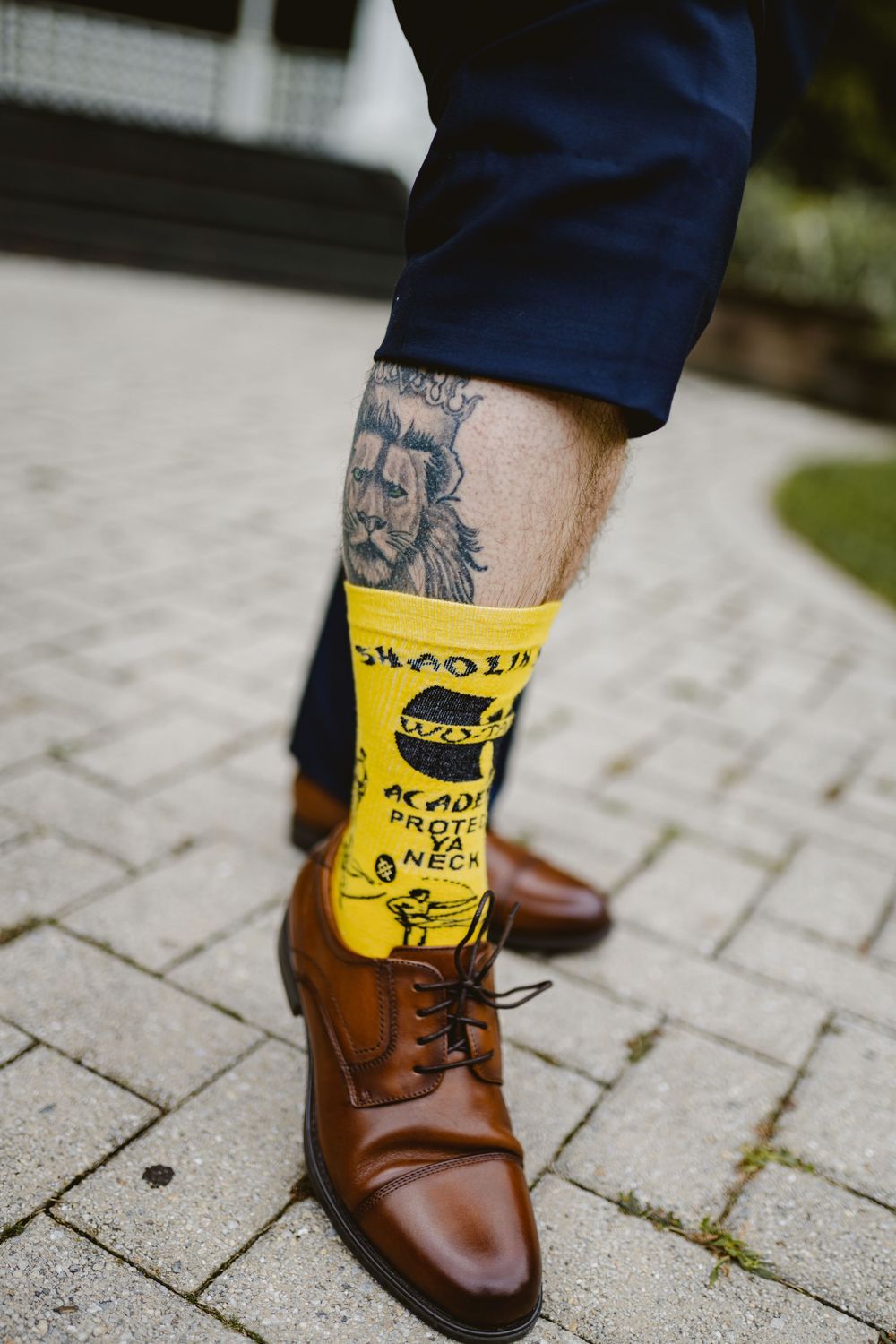 Close-up of brown leather dress shoe and yellow novelty sock with leg tattoo visible.