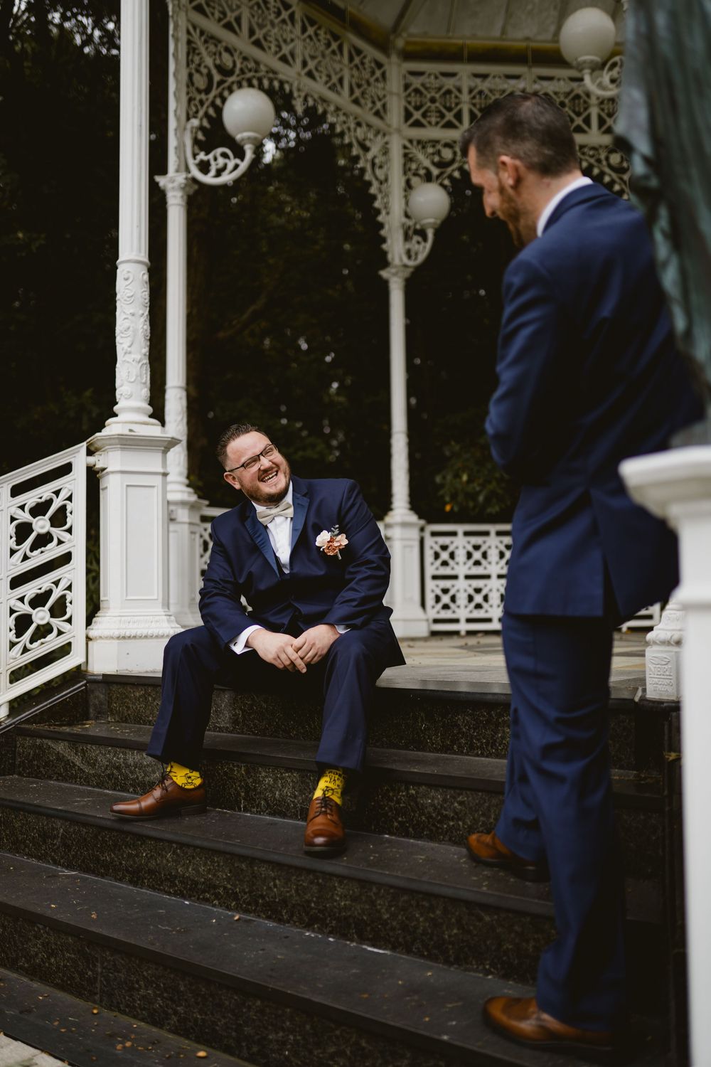 Two people in navy suits share lighthearted moment on gazebo steps.