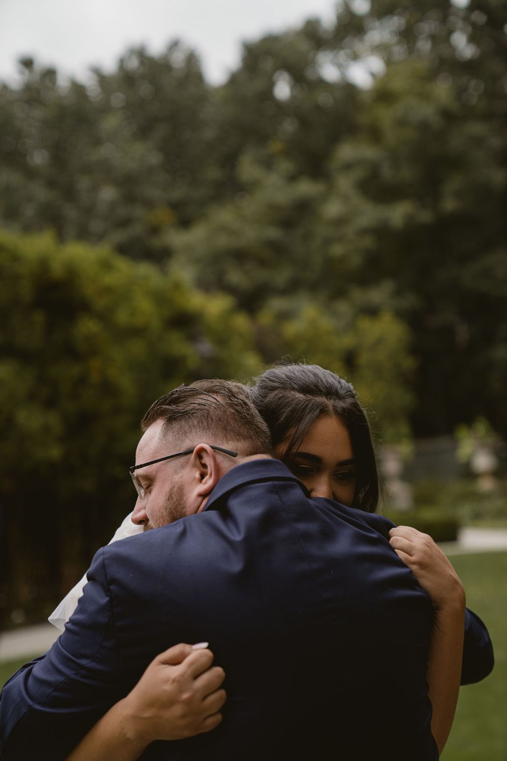 Two people share emotional embrace at outdoor garden wedding.