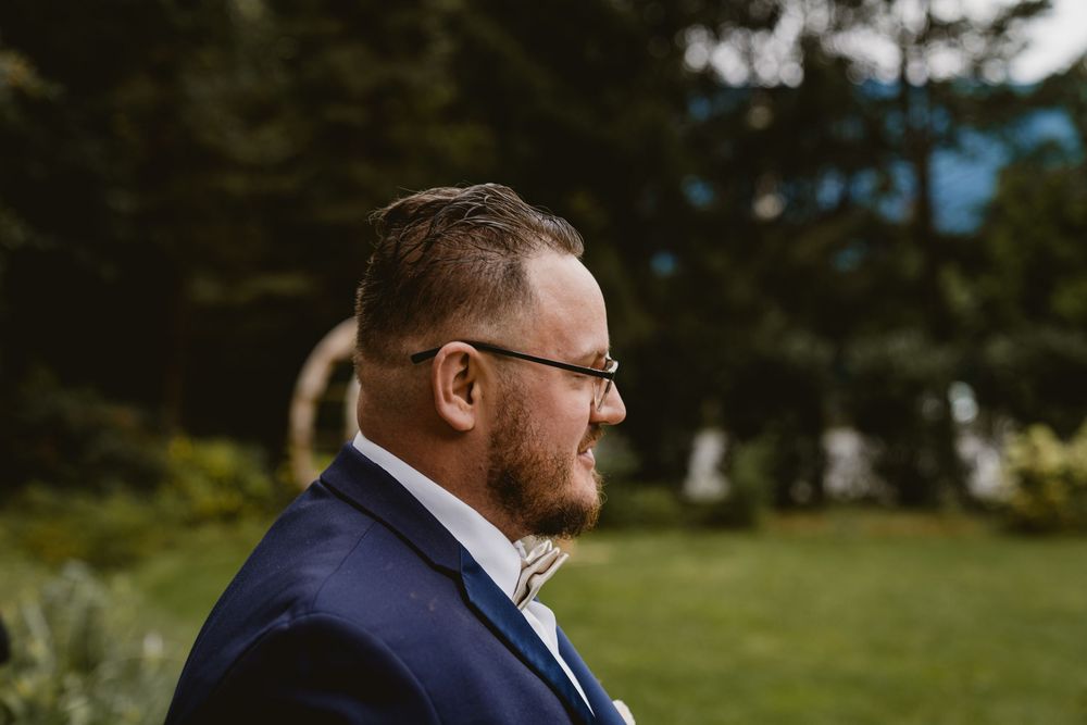 Side profile of person in navy suit and glasses at outdoor wedding.