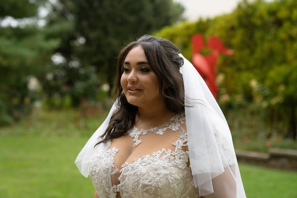 Bride in lace wedding gown with veil poses in garden setting.