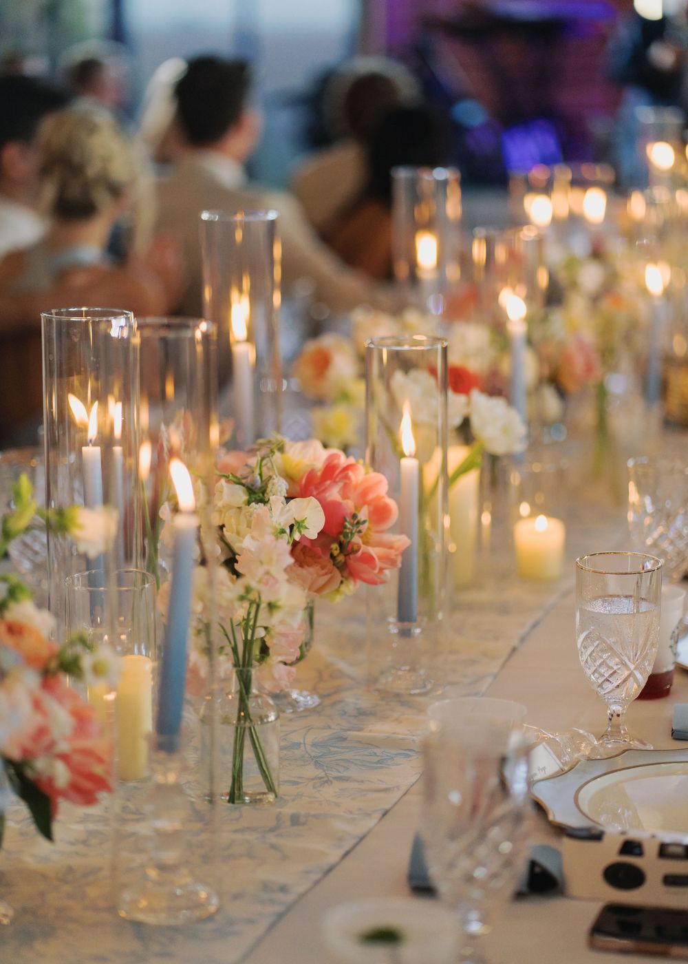 Elegant wedding reception table with tall candles, pink tulips, and white floral arrangements.