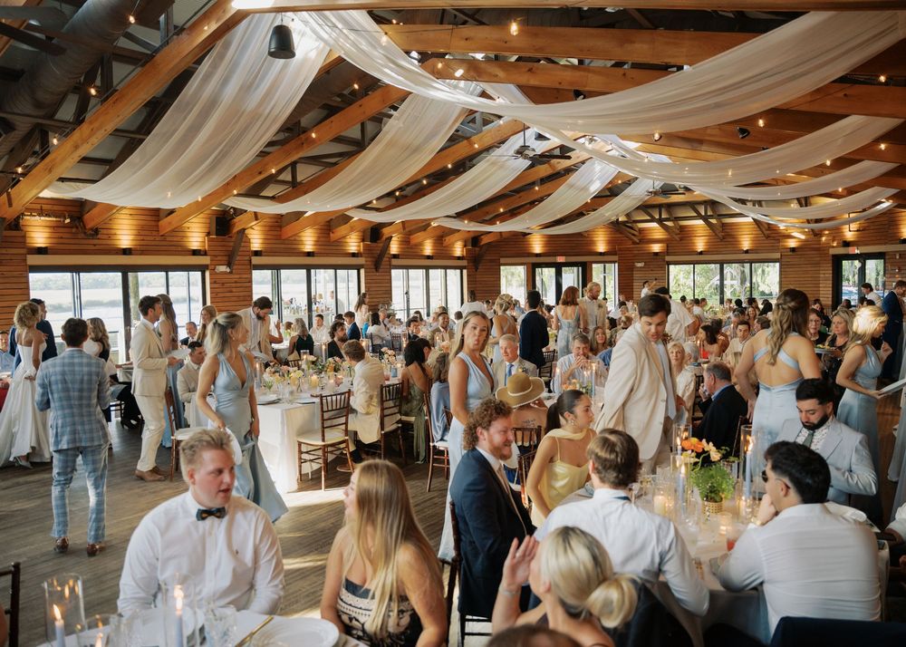 Guests mingling at a wedding reception in a rustic barn venue with draped white ceiling decor.