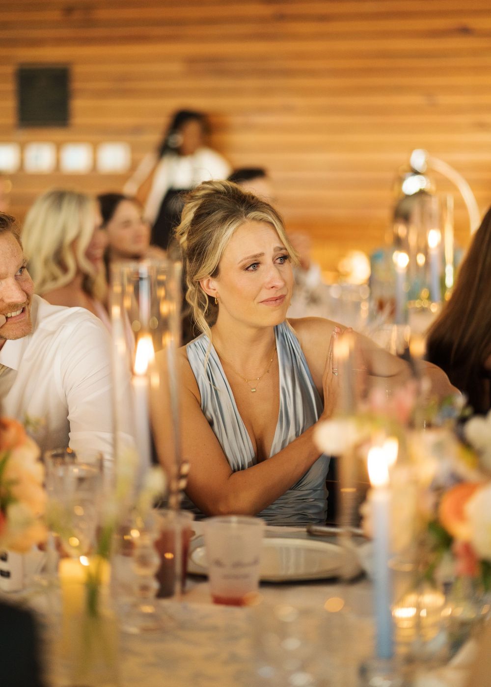 Emotional bridesmaid in blue dress crying during wedding reception speech at candlelit dinner table.