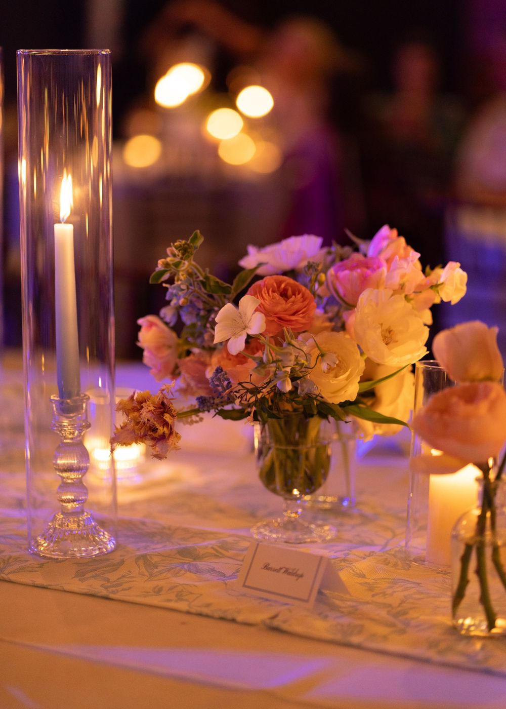 Elegant wedding table centerpiece with colorful blooms and tall candles in warm candlelight.