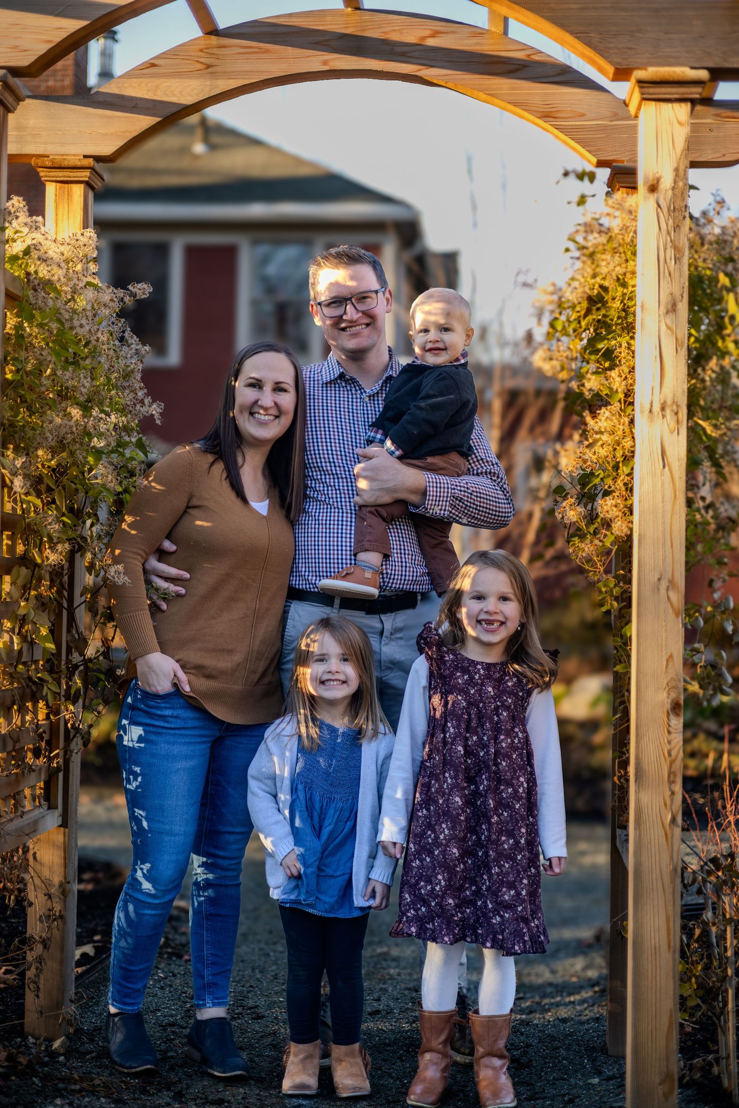 Candid family portrait under a wooden pergola during autumn with golden foliage in the background.