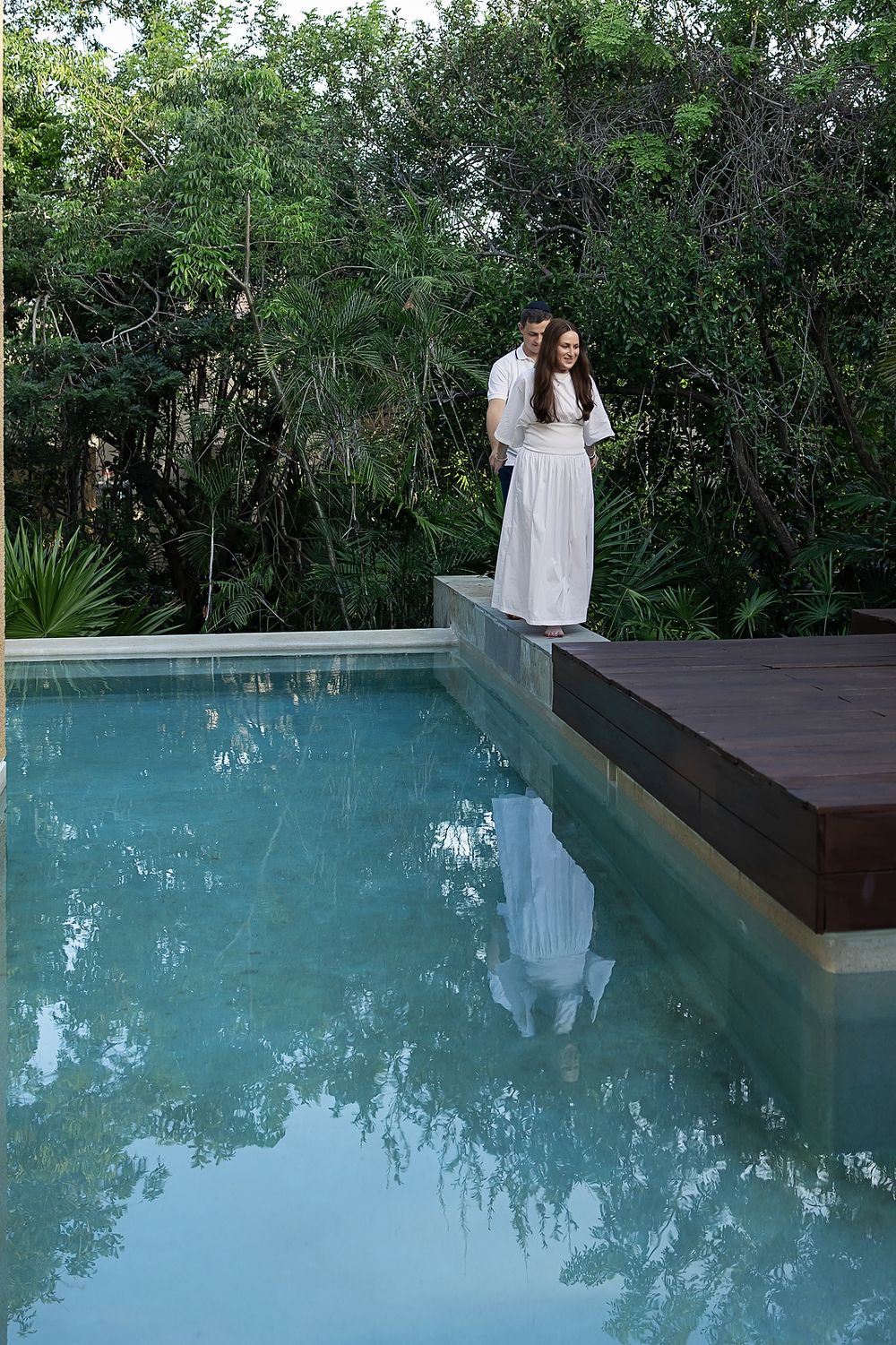Person reflected in an infinity pool surrounded by lush tropical greenery at a luxury resort.