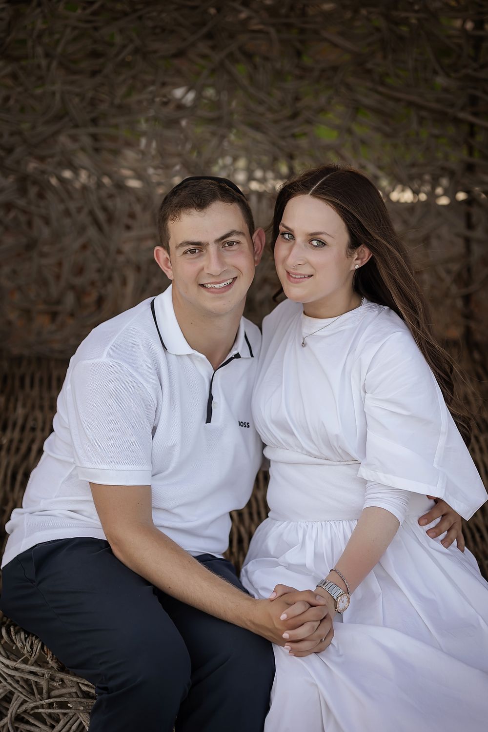 A couple in white clothing sits together for a romantic portrait outdoors.