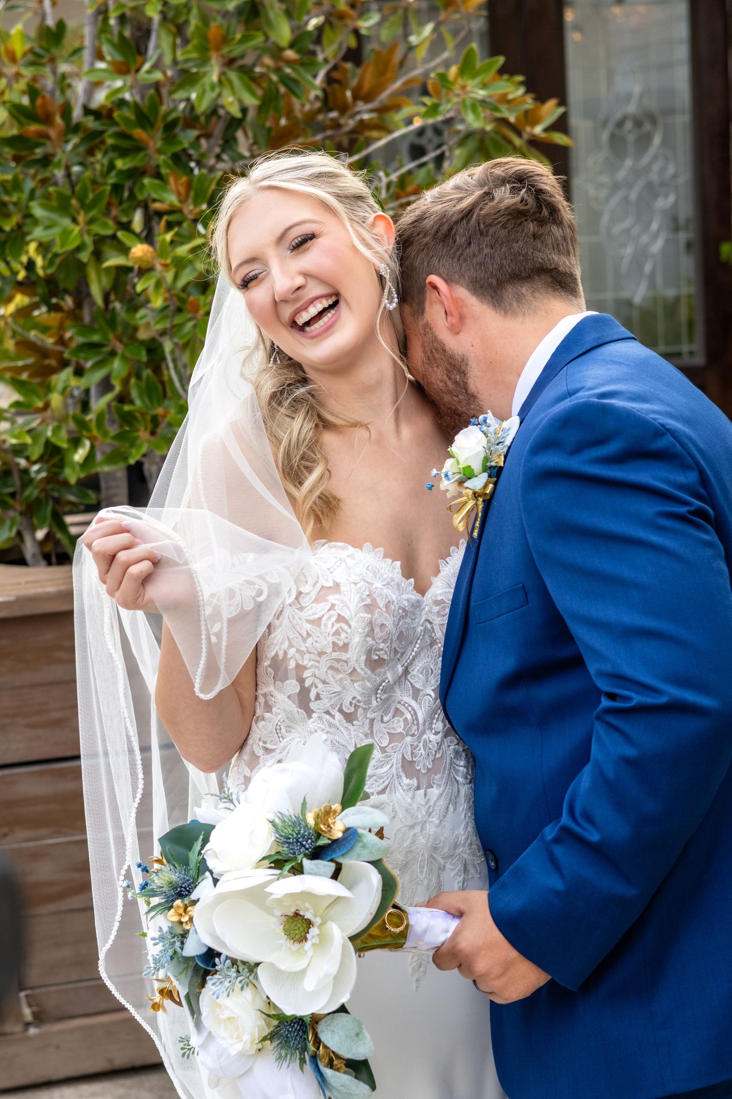 Joyful wedding couple sharing laughs while holding a white floral bouquet.