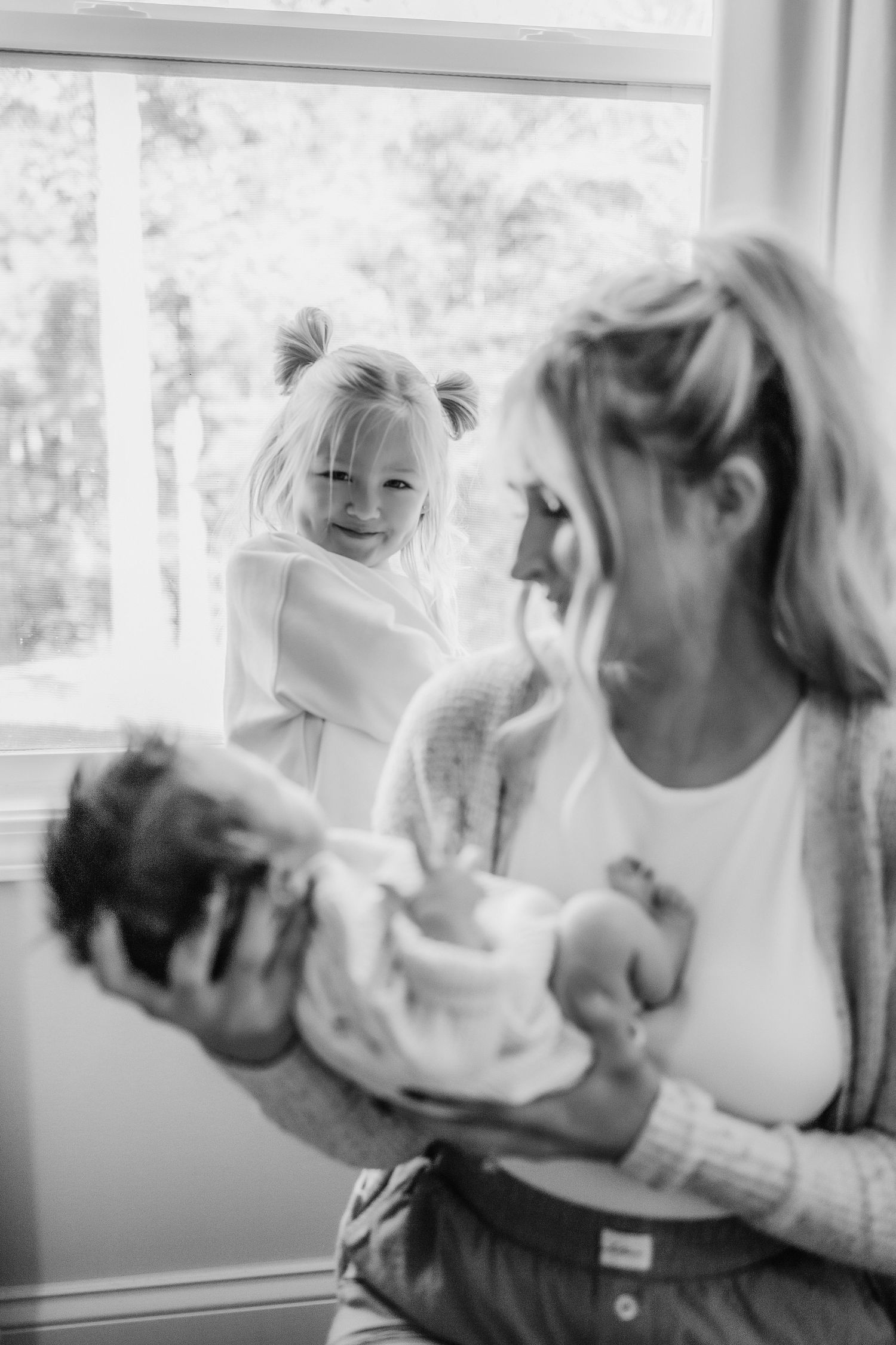 Black and white photo of a tender family moment between parents and their small infant baby near a window.