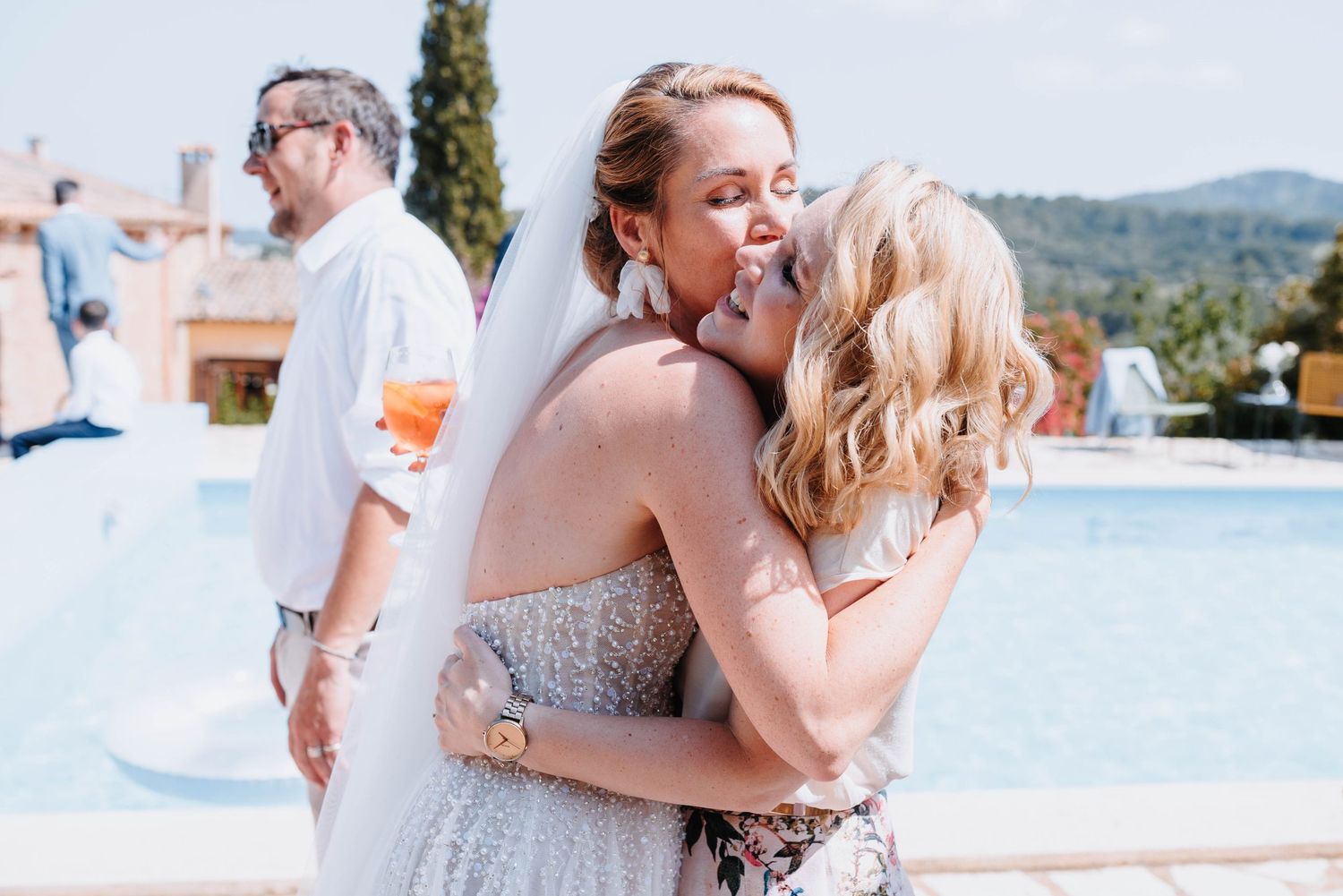 Inniger Moment als die Schwester der Braut ihr gratuliert und die Braut ihre Schwester auf die Wange küsst vor Freude am Pool ihrer Finca.