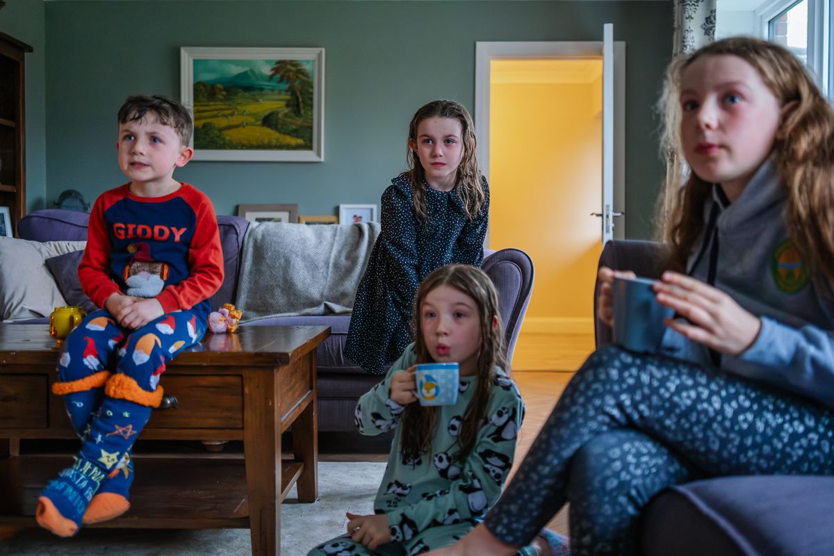 Family group gathered in a living room wearing casual clothes while watching something together.