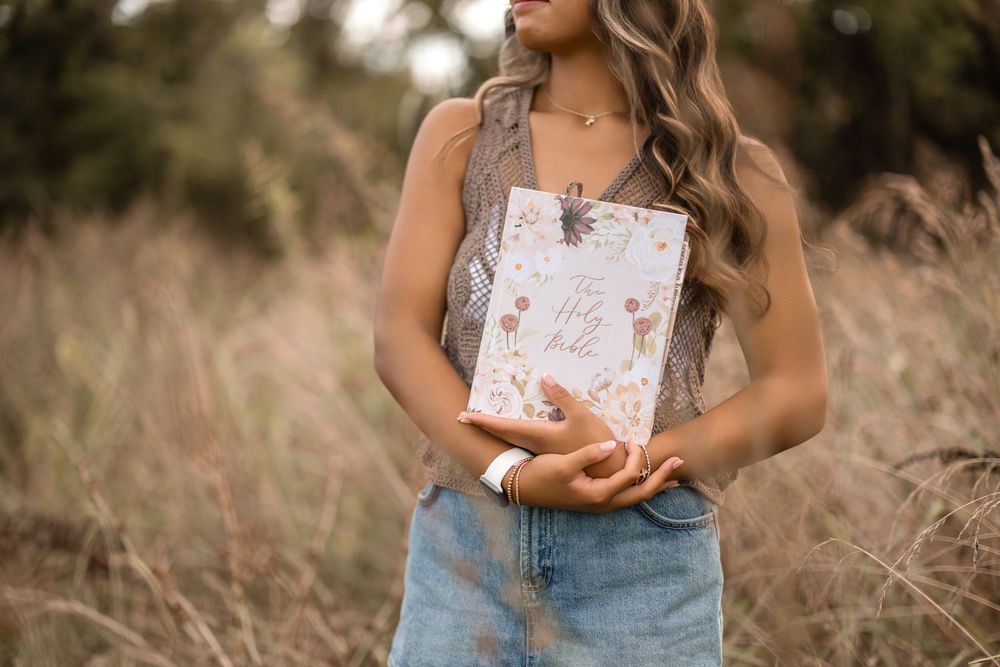 Woman in denim skirt holding floral book or journal in outdoor field setting.