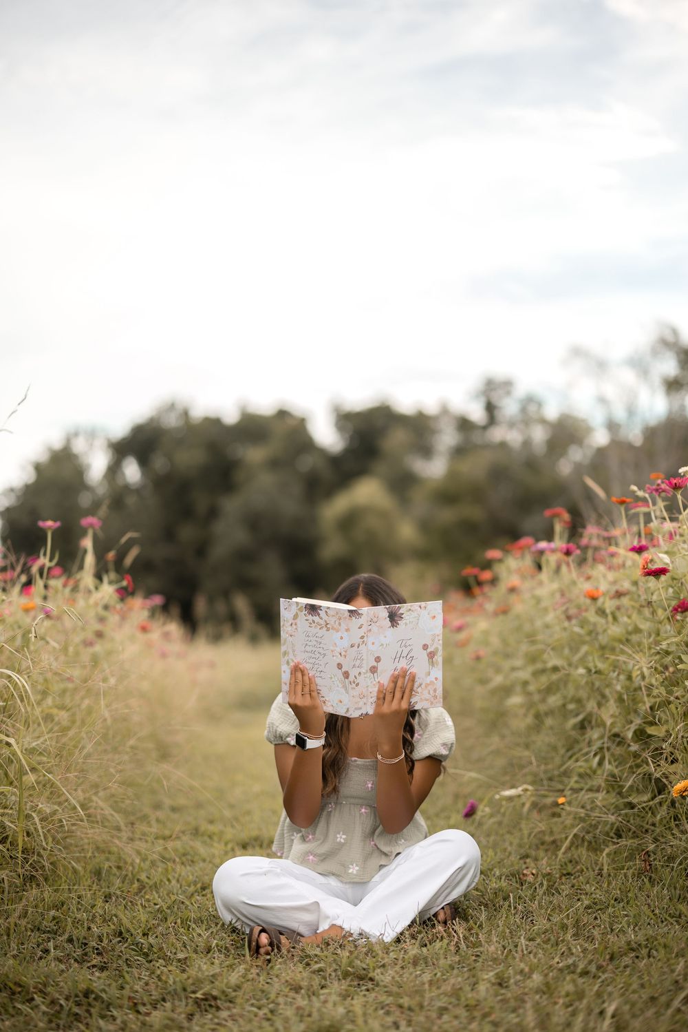 Someone relaxes in a wildflower field while reading a book on a sunny afternoon.