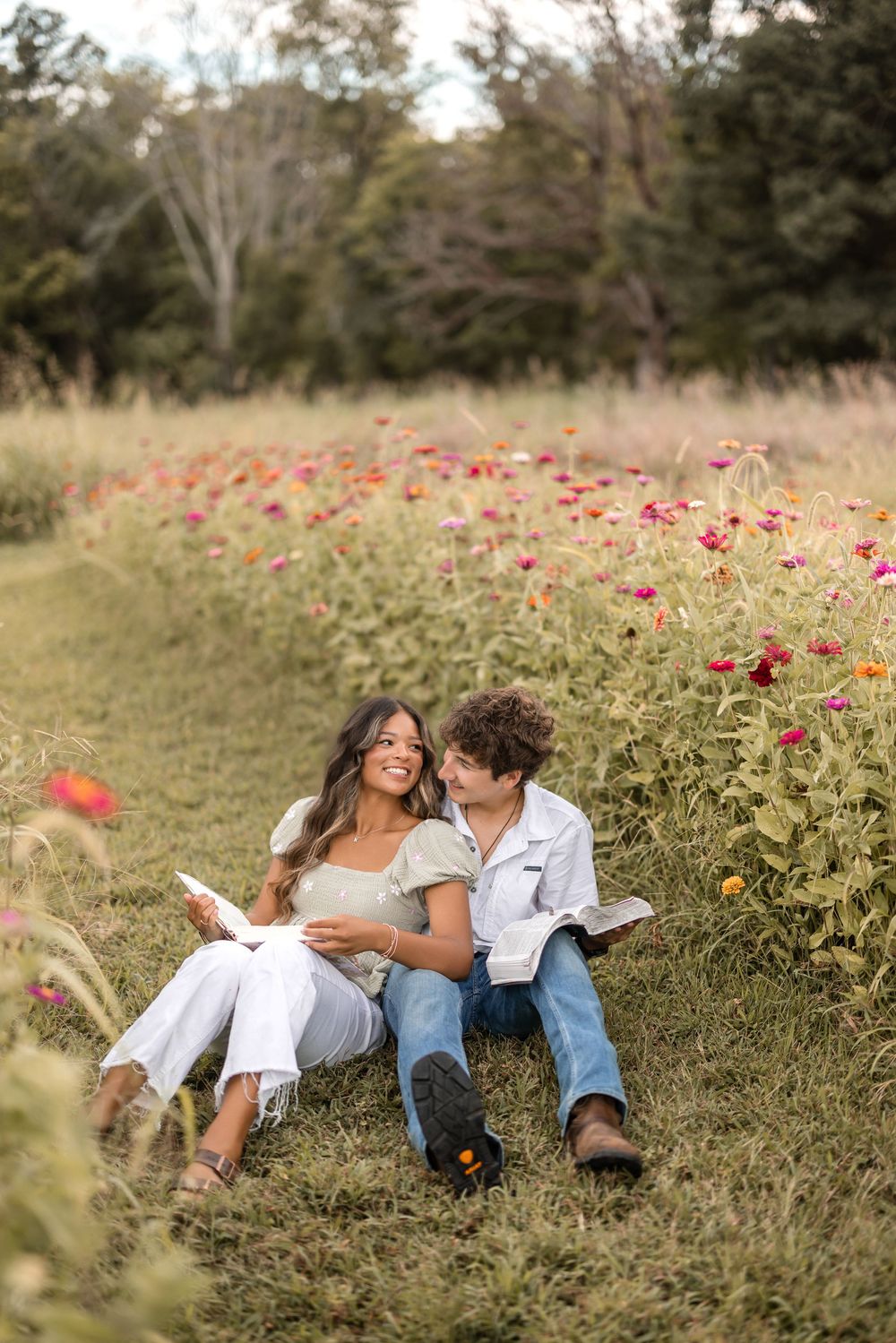 A couple relaxes together reading in a meadow with blooming red wildflowers on a sunny afternoon.