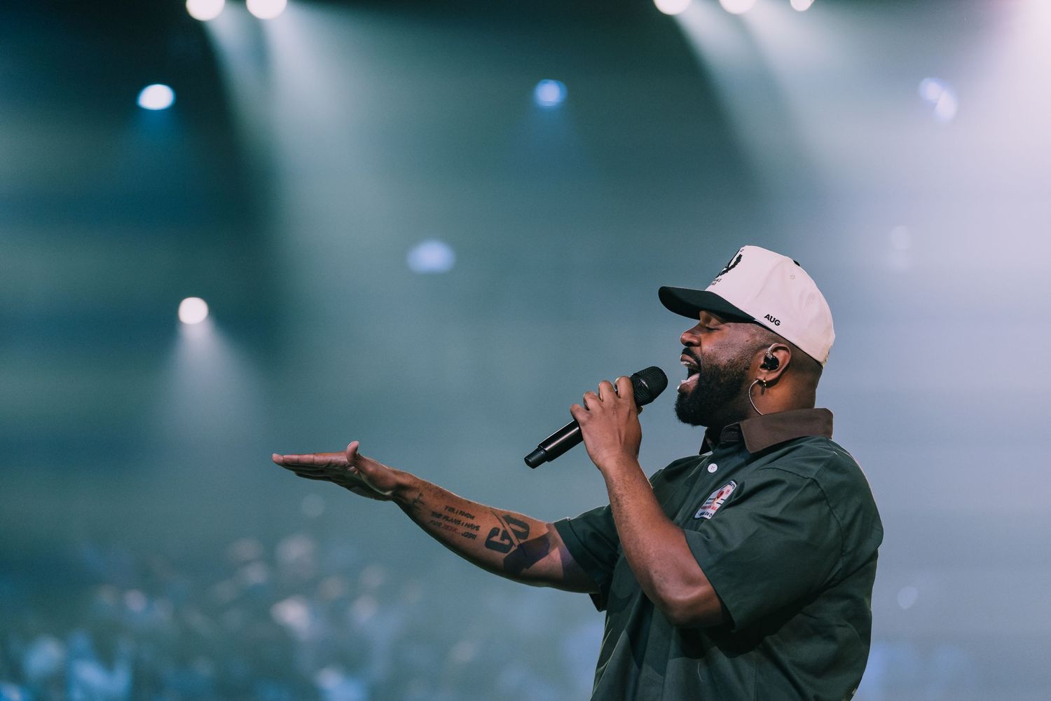 Tattooed male rapper performing on stage with microphone under dramatic concert lighting.