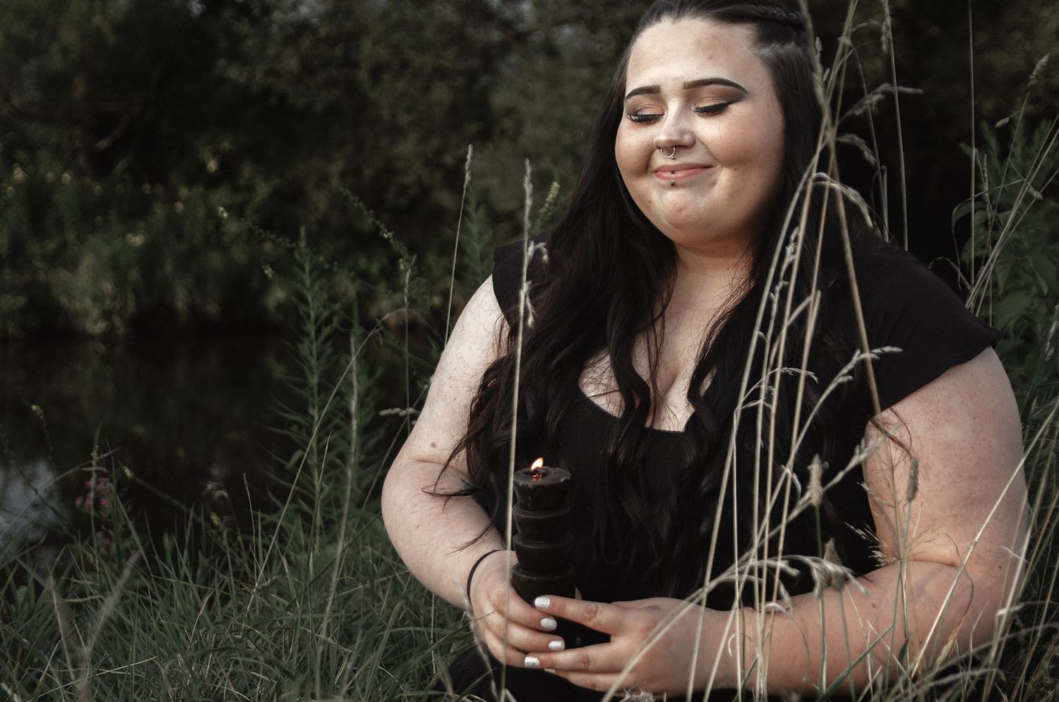 A moody outdoor portrait of someone in black clothing among tall grasses at dusk.