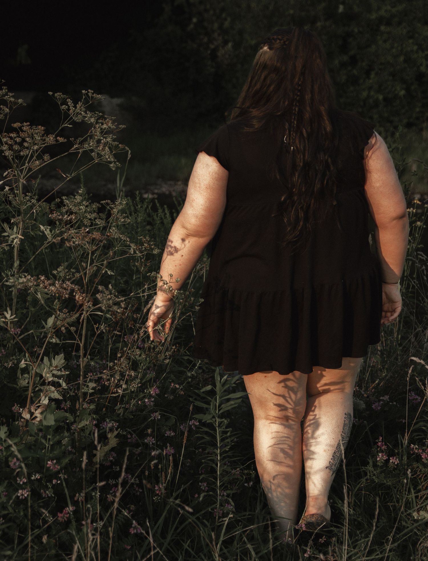 Full-length portrait showing flowing black dress against wild garden foliage.