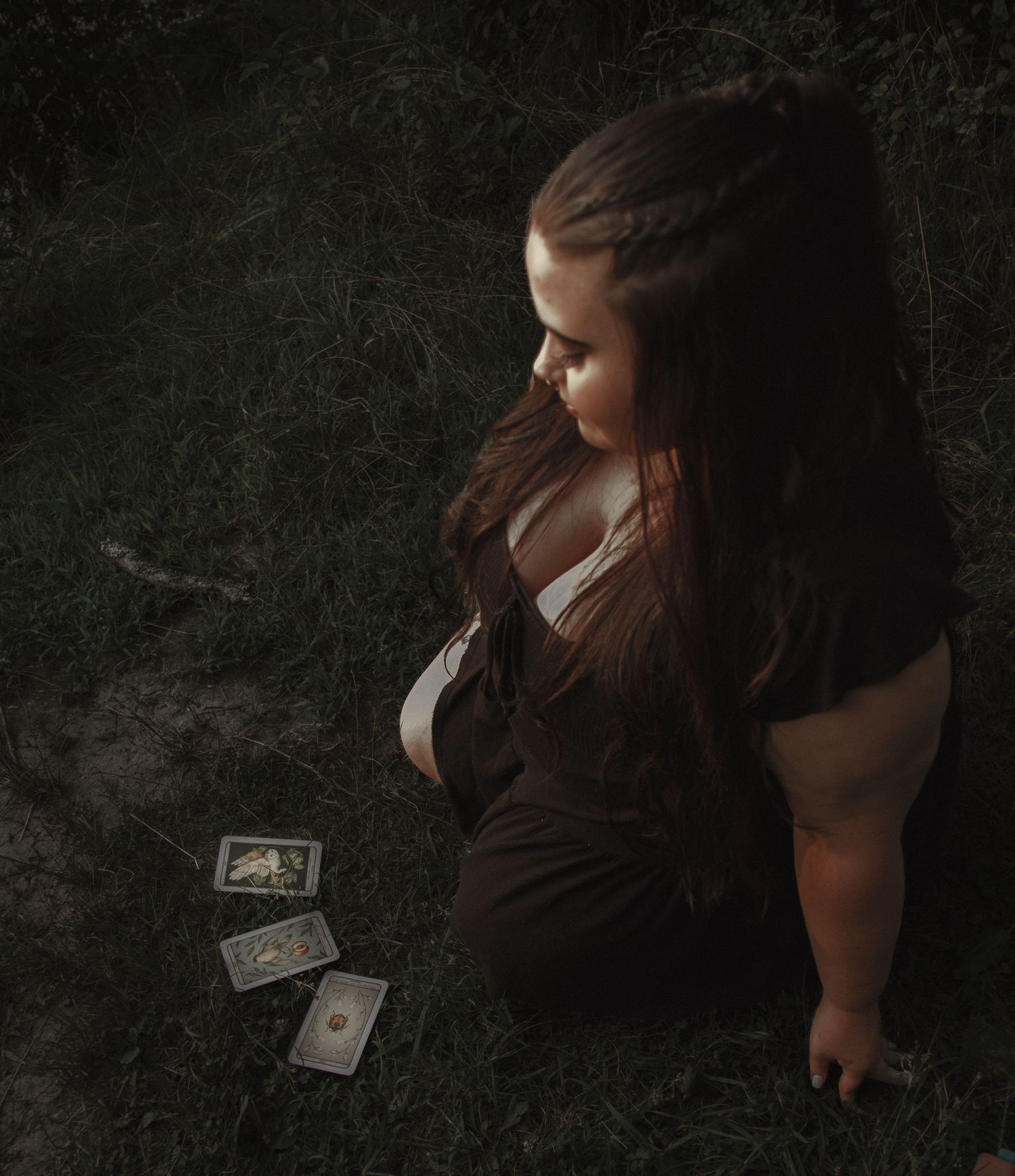 Artistic portrait with playing cards scattered on dark grass in moody lighting.