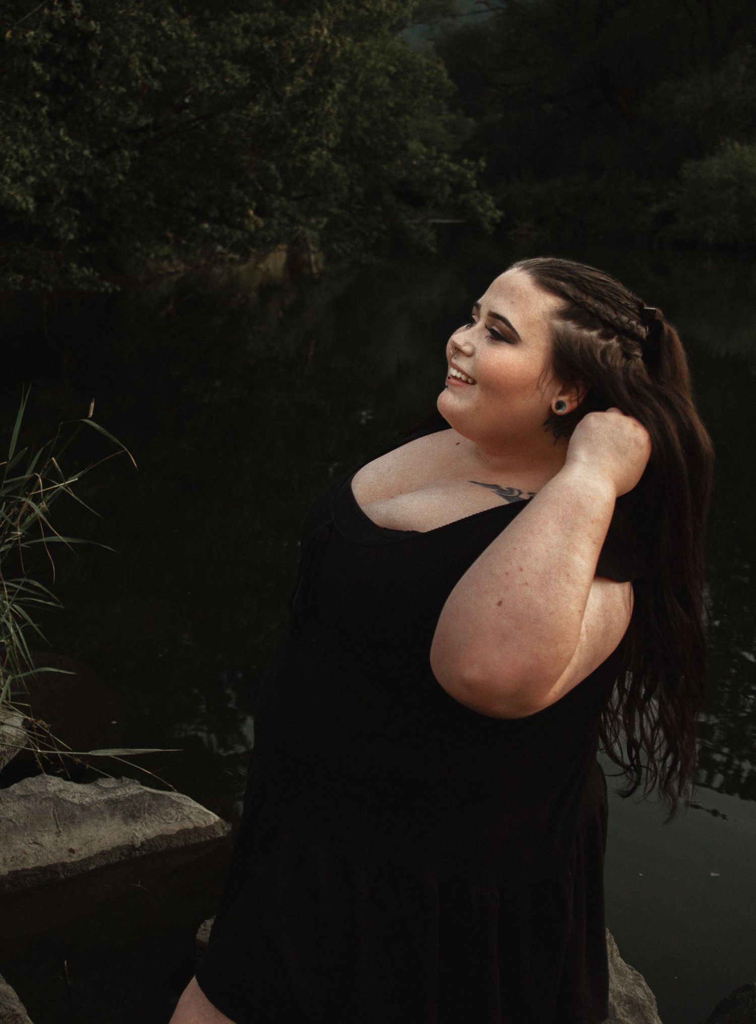 Candid outdoor portrait by a lake with person in black dress adjusting hair.