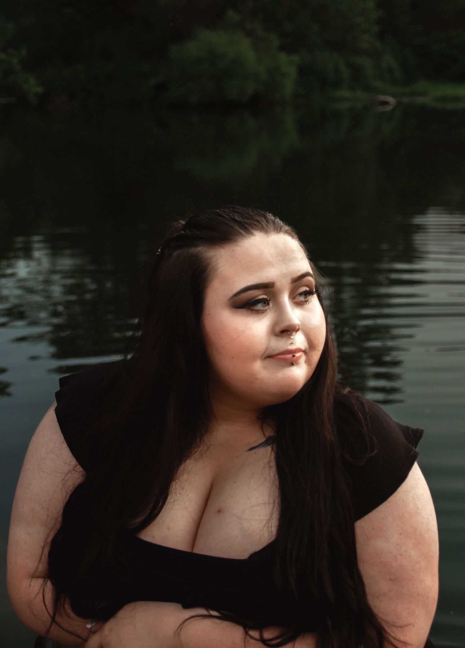 Stylish portrait in black dress against reflective water backdrop.