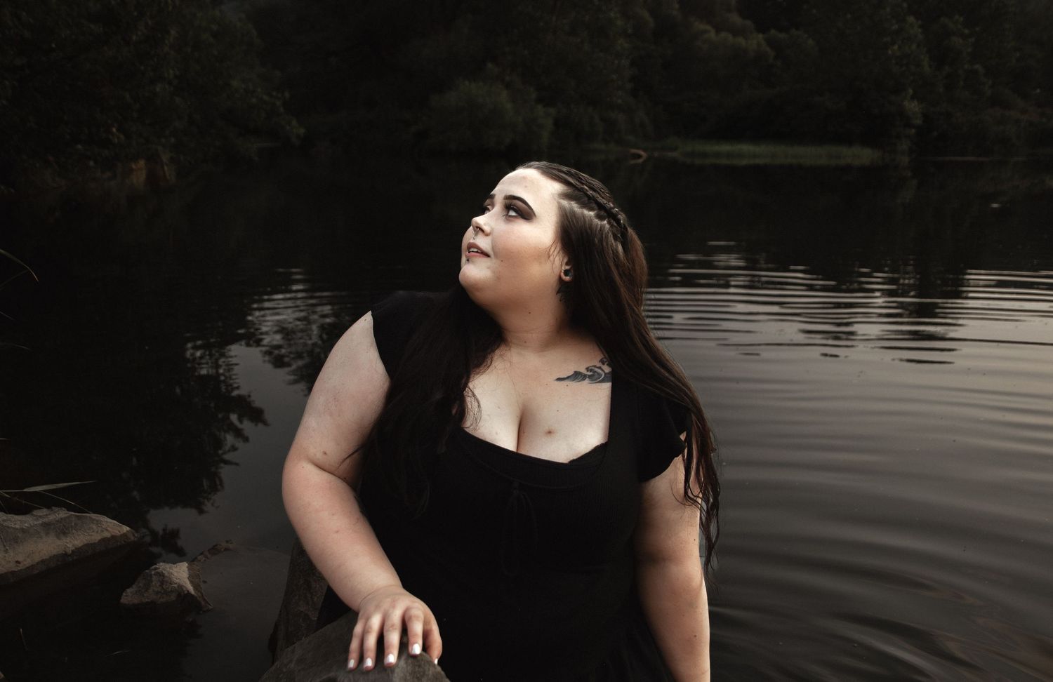 Artistic portrait by water featuring black dress and natural lighting.