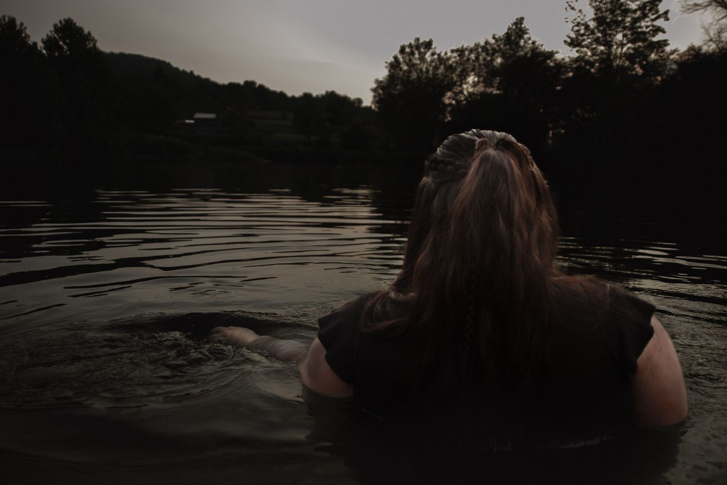 Silhouette in water during sunset with mountains and trees in background.