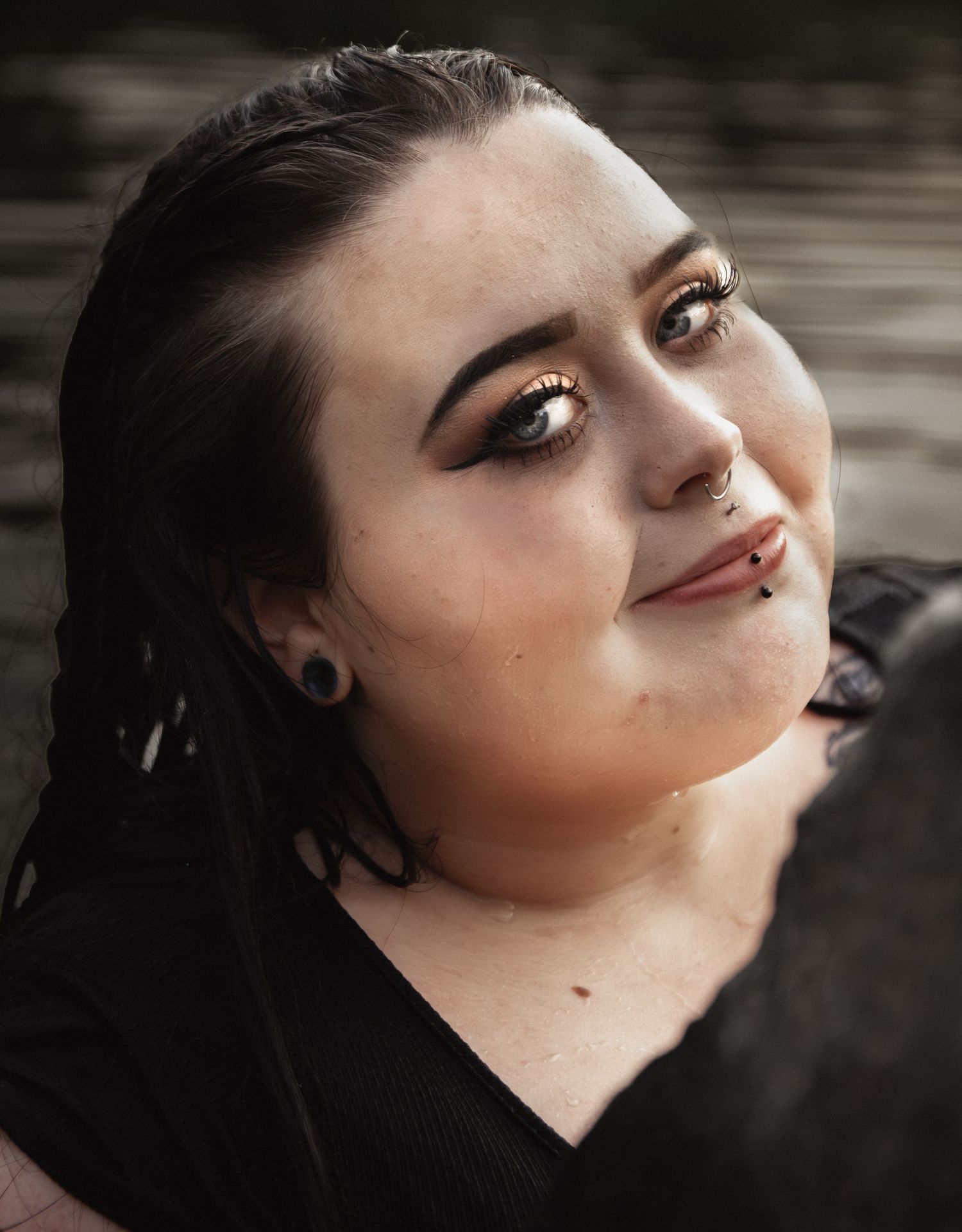 Close up beauty portrait with dramatic eye makeup and nose piercing against blurred background.