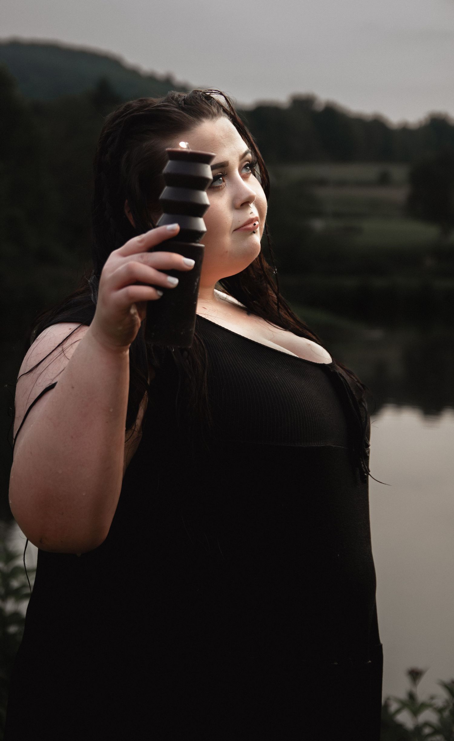 Fashion portrait holding dark tumbler against lake landscape in evening light.
