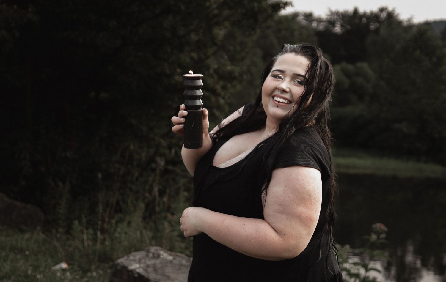Casual outdoor portrait holding beverage container with natural scenery background.