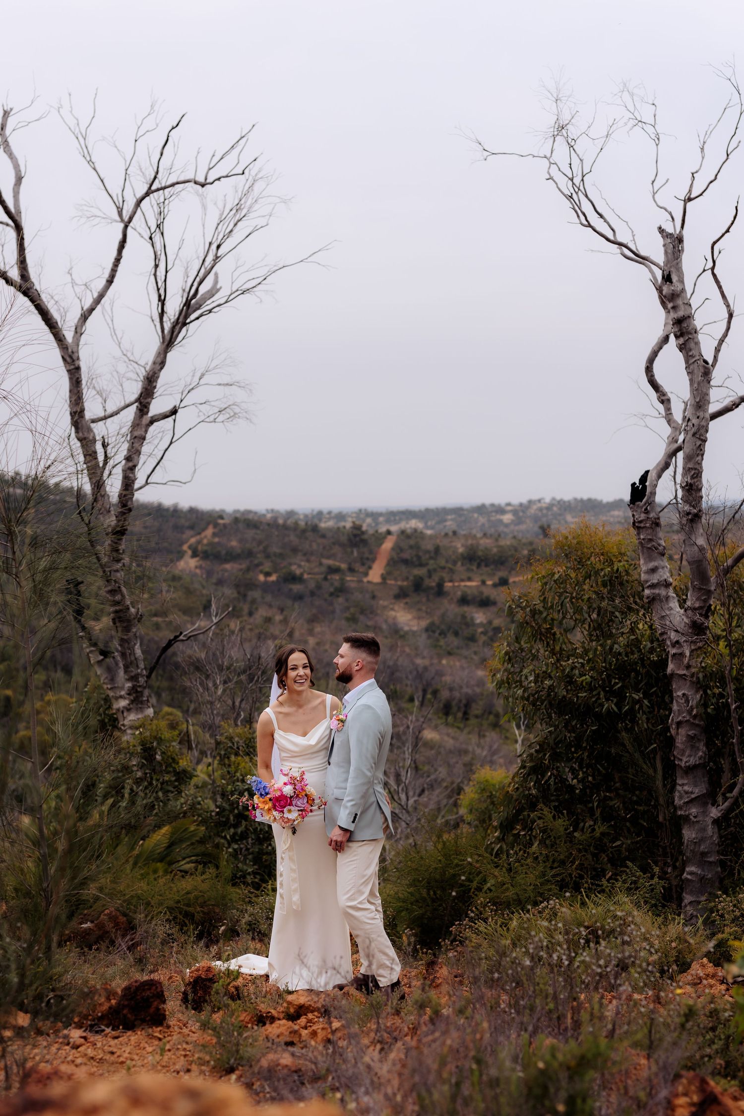 Three side-by-side landscape photos show a romantic couple in wedding attire standing among bare desert trees and brush.