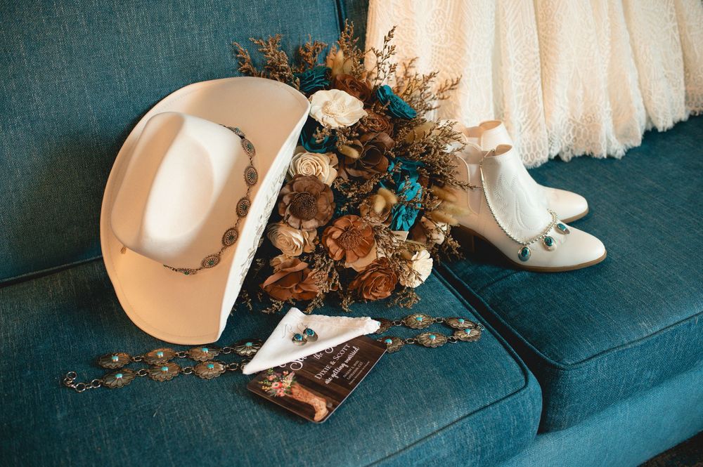 A series of wedding items arranged on a teal surface including flowers, belts, perfume bottles, and accessories.
