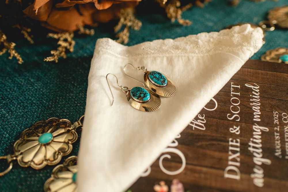 Elegant turquoise and gold earrings displayed on a white cloth napkin beside vintage decor and book.