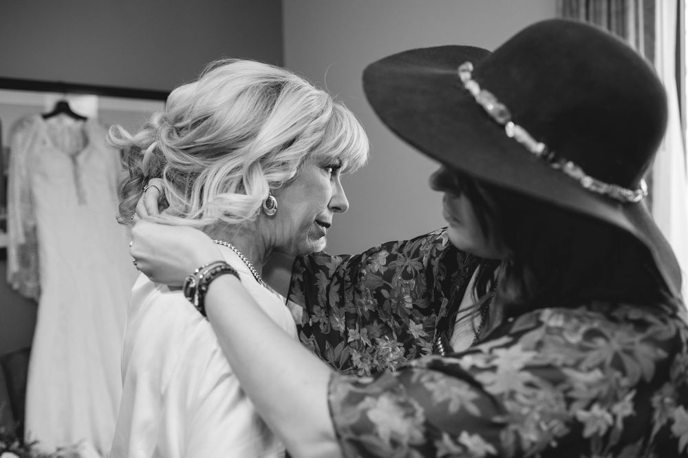 Black and white photo showing intimate bridal preparation moment with styling assistance in a dressing room.