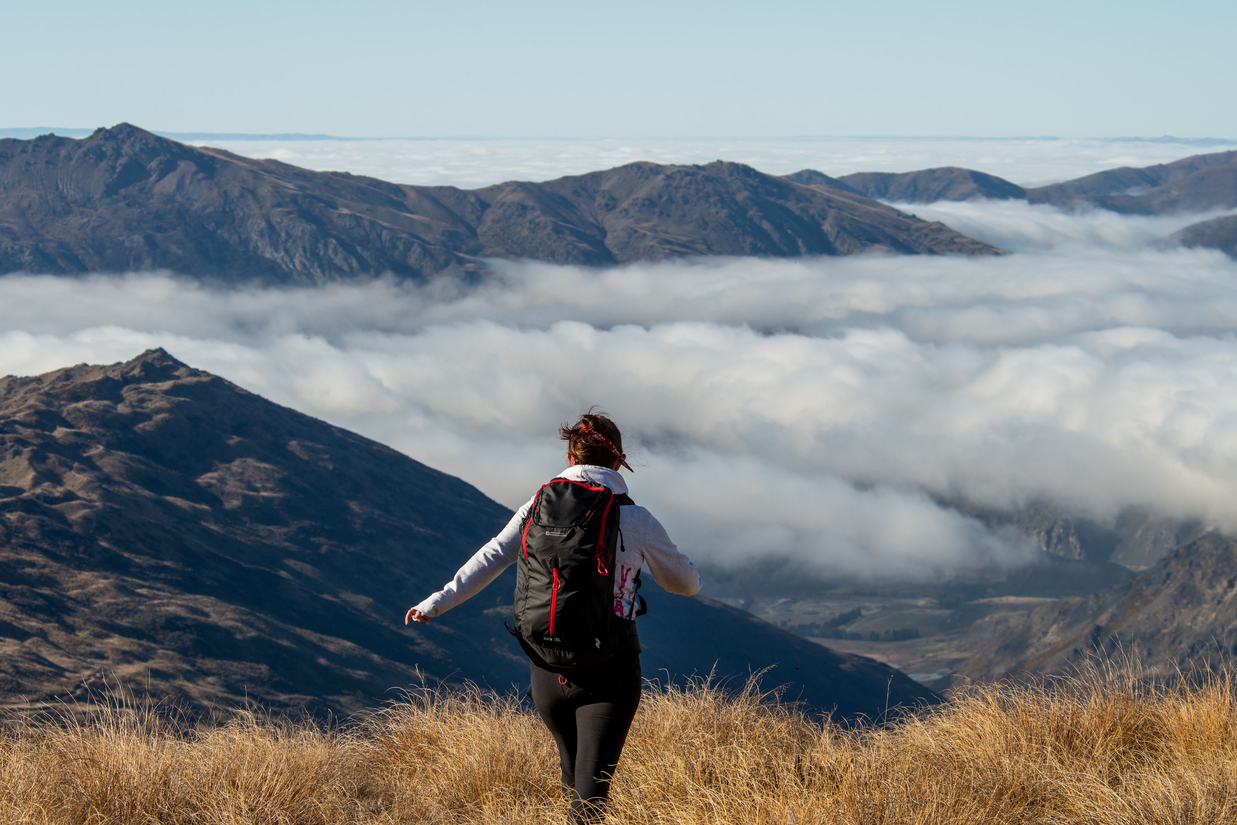 Randonnée en Nouvelle-Zélande, femme de dos face à une mer de nuages et montagnes sauvages