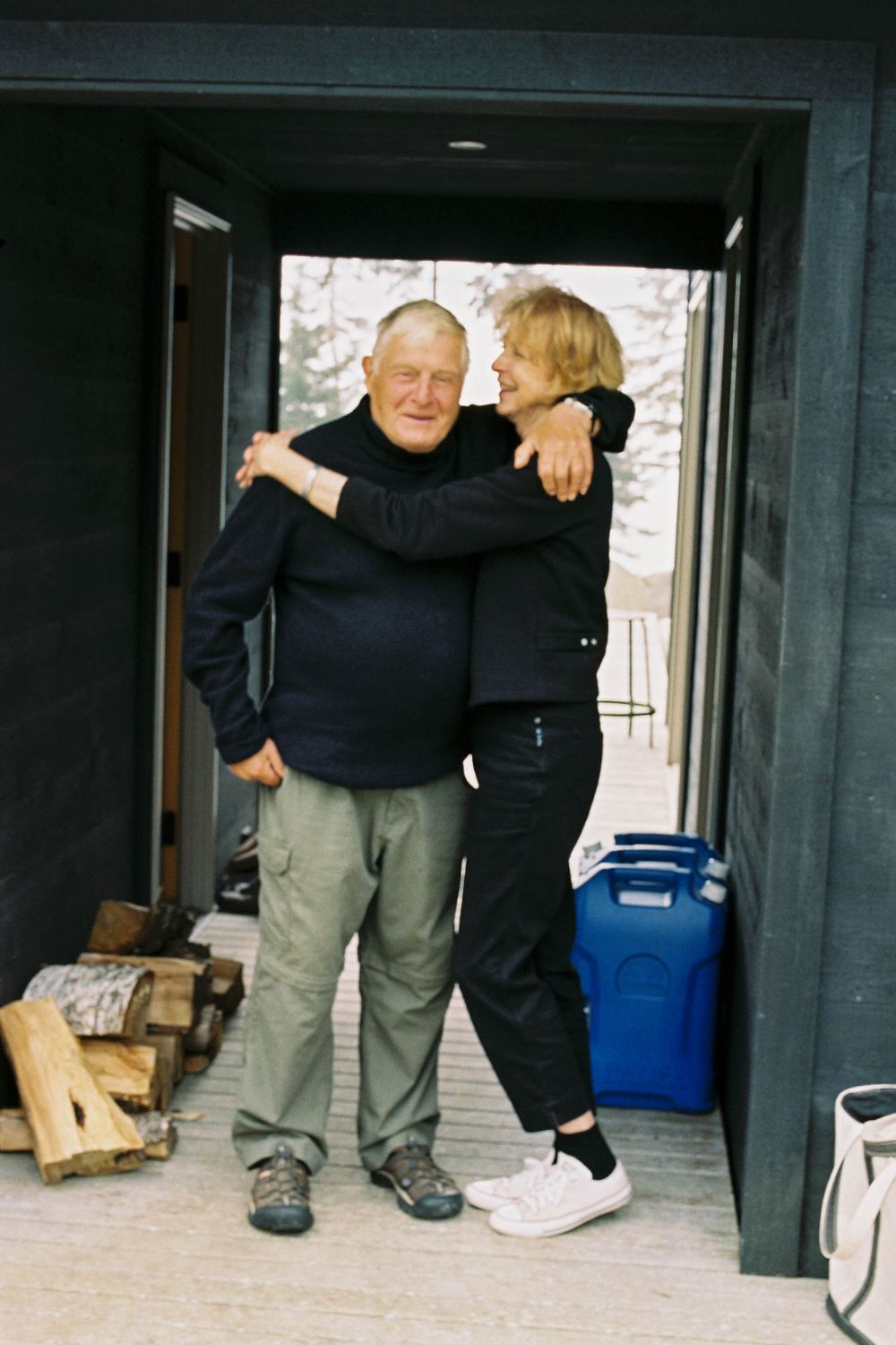 Candid photo of a couple holding onto each other on the front porch of their island home near Thomaston, Maine.