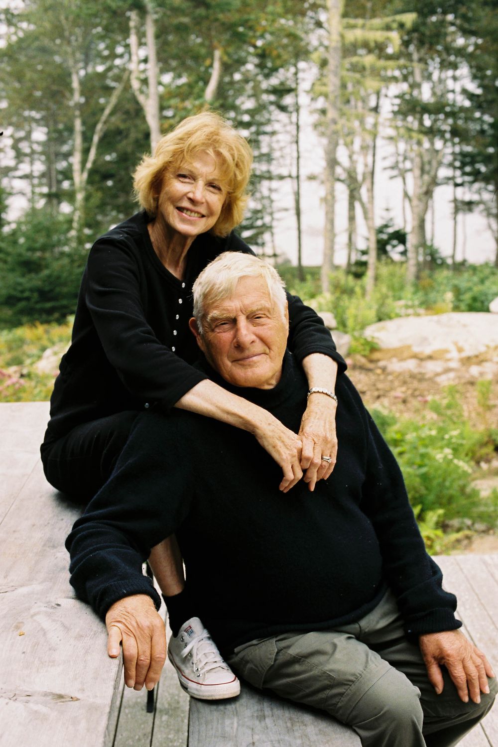 A couple poses together on a picnic table outside their home in the late summer on an island off the coast of Maine.